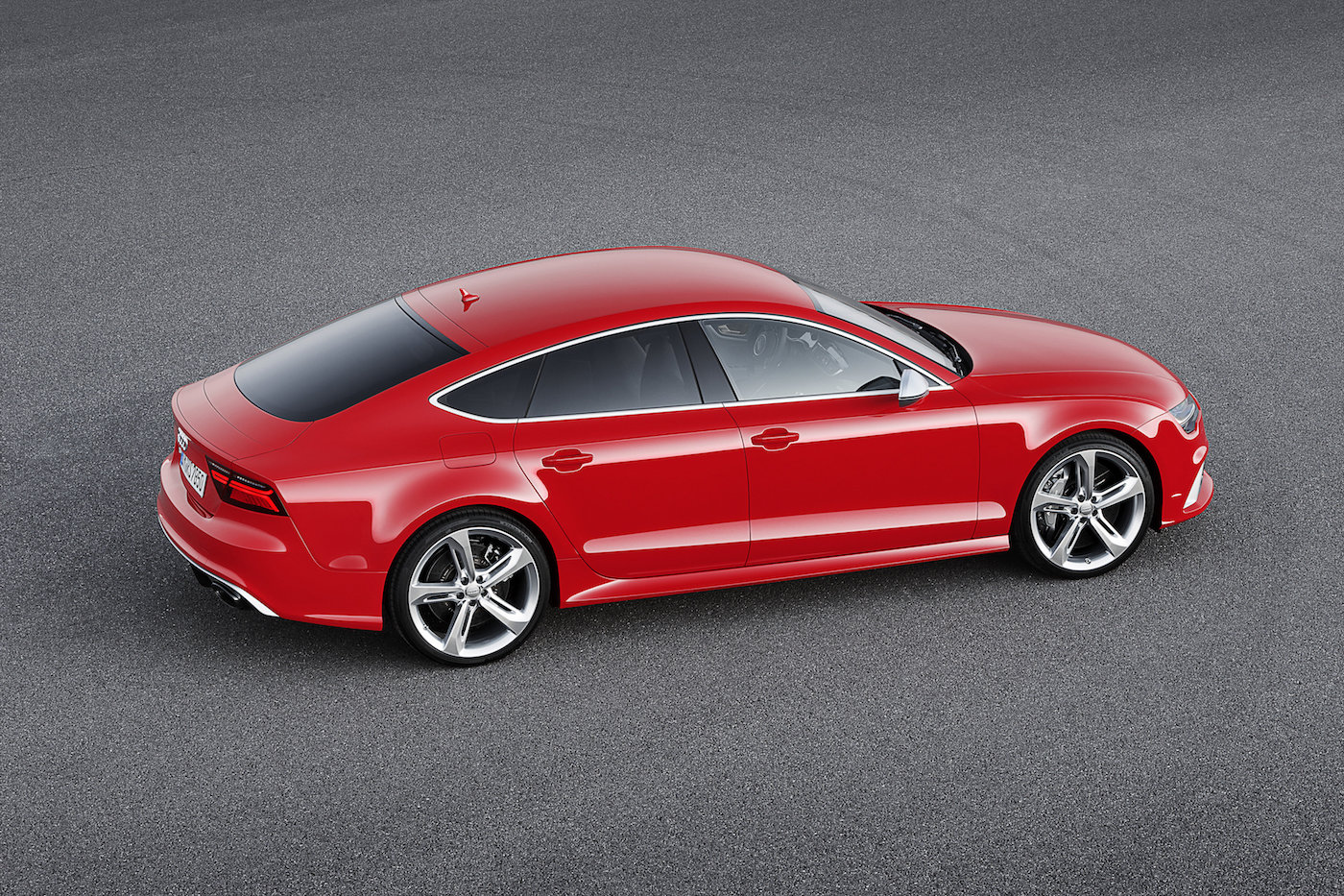 Rotes Sport-Coupé mit schwarzen Fenstern, silbernen Felgen und elegantem Design auf grauem Asphalt. Seitenansicht von schräg oben.