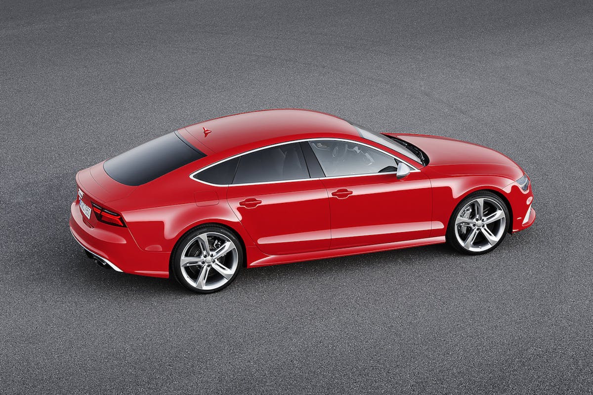 Rotes Sport-Coupé mit schwarzen Fenstern, silbernen Felgen und elegantem Design auf grauem Asphalt. Seitenansicht von schräg oben.