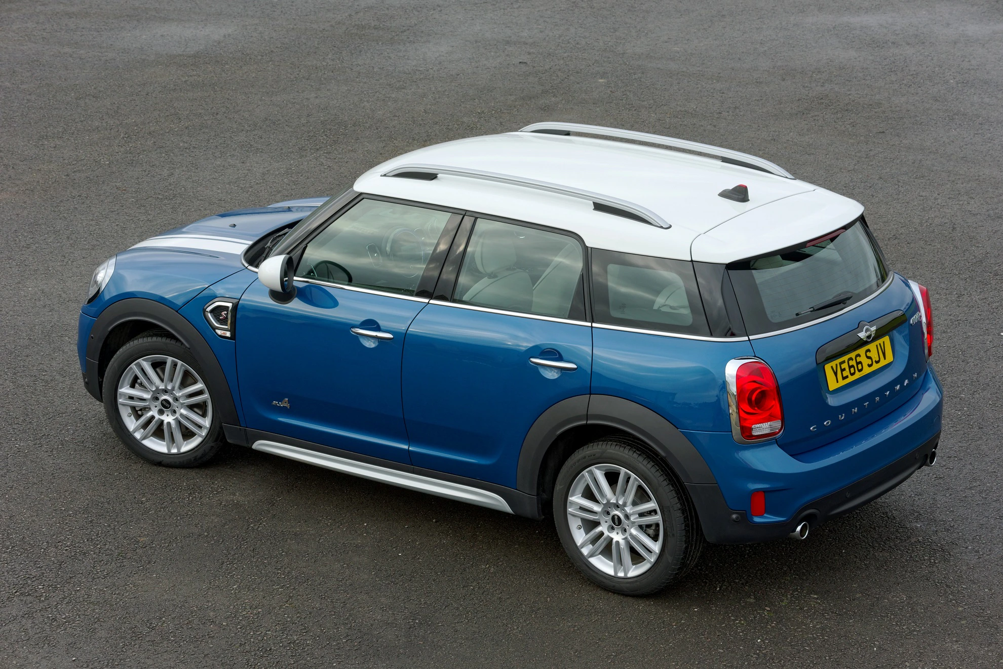 Blauer Mini Cooper mit weißem Dach, Dachreling und UK-Kennzeichen auf Asphalt geparkt, seitliche und obere Perspektive.