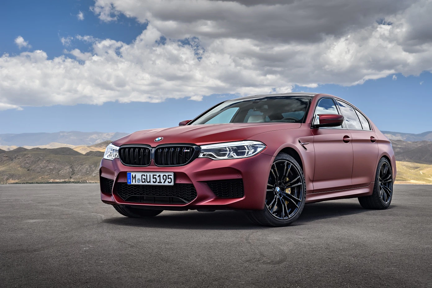 Roter BMW-Sportwagen steht auf einer Straße vor einer gebirgigen Landschaft unter bewölktem Himmel.