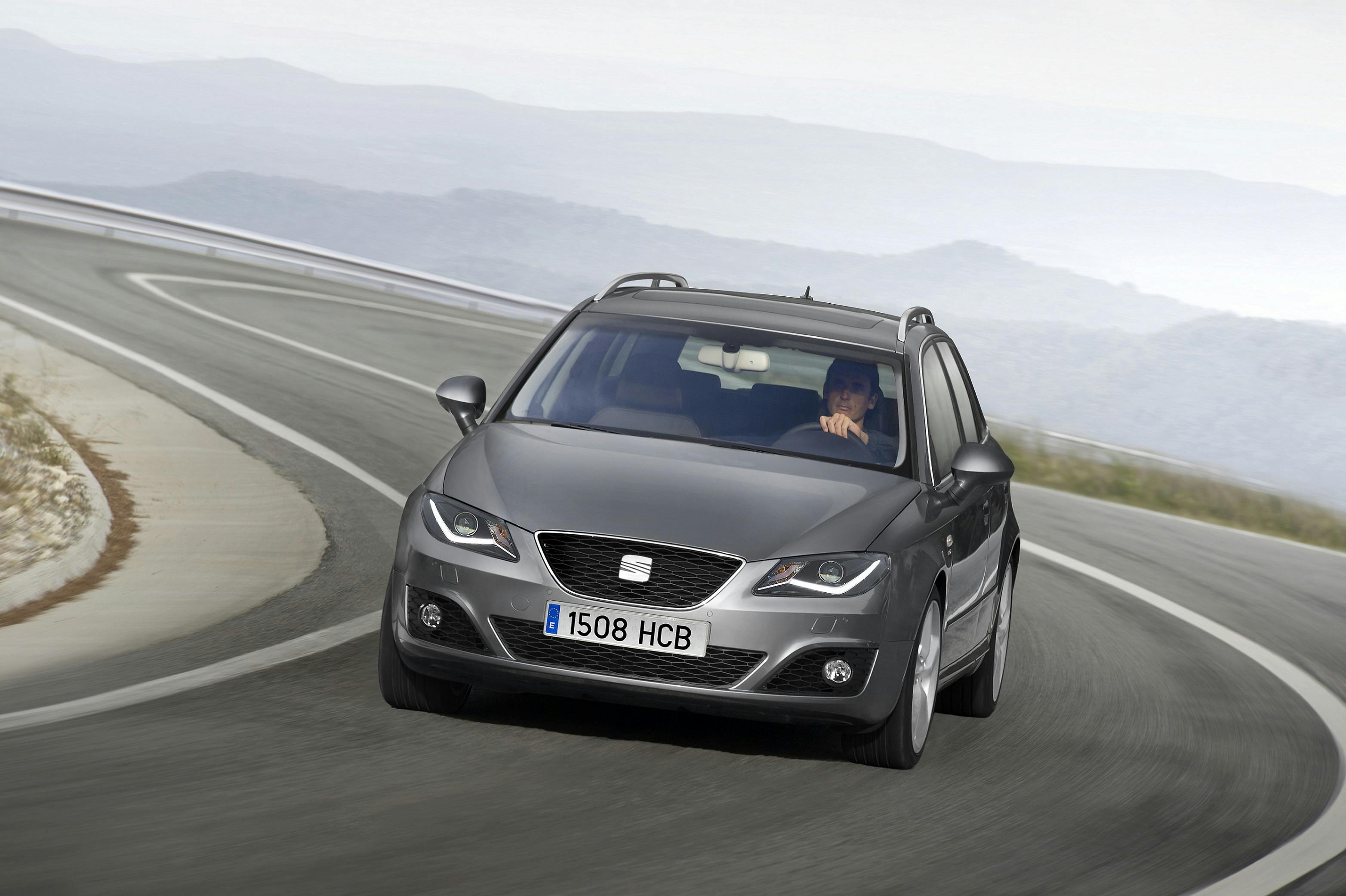 Silberner Kombi fährt auf einer kurvigen, leeren Landstraße entlang einer Hügelkette. Fahrer mit beiden Händen am Lenkrad.