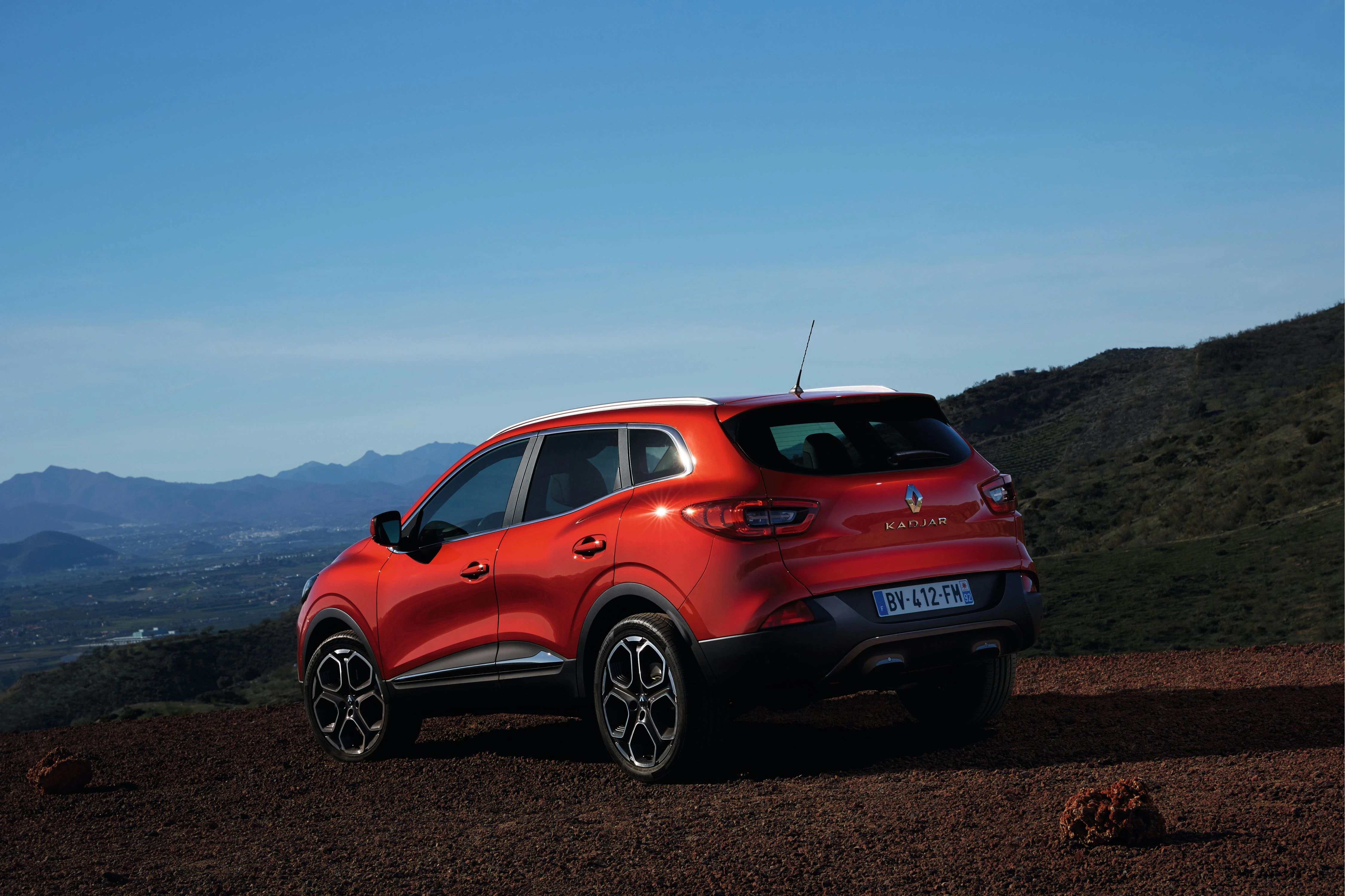 Roter SUV steht in bergiger Landschaft mit klarem Himmel. Die Kennzeichen sind sichtbar. Hintergrund bietet weiten Blick über Hügel und Tal.