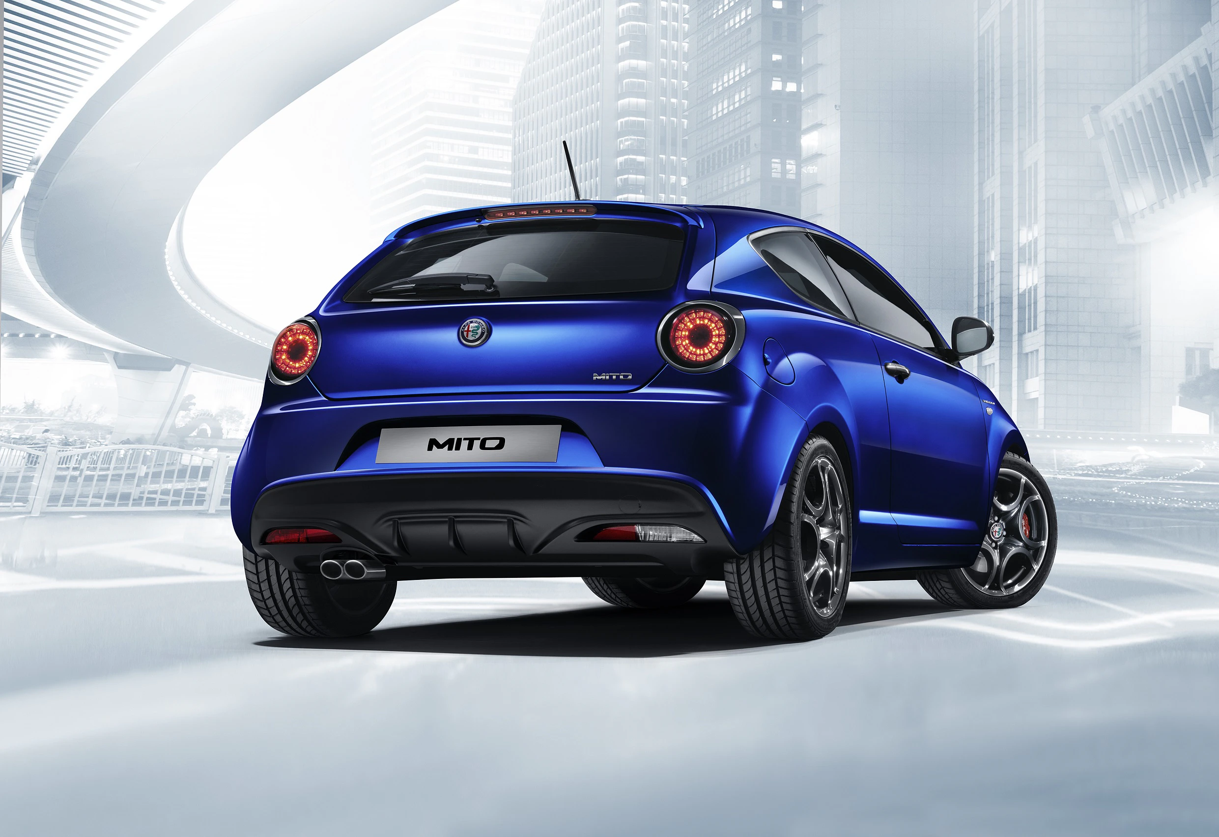 Blauer Alfa Romeo MiTo von hinten, geparkt in einer futuristischen Stadtumgebung mit geschwungenen Brücken und modernen Gebäuden.