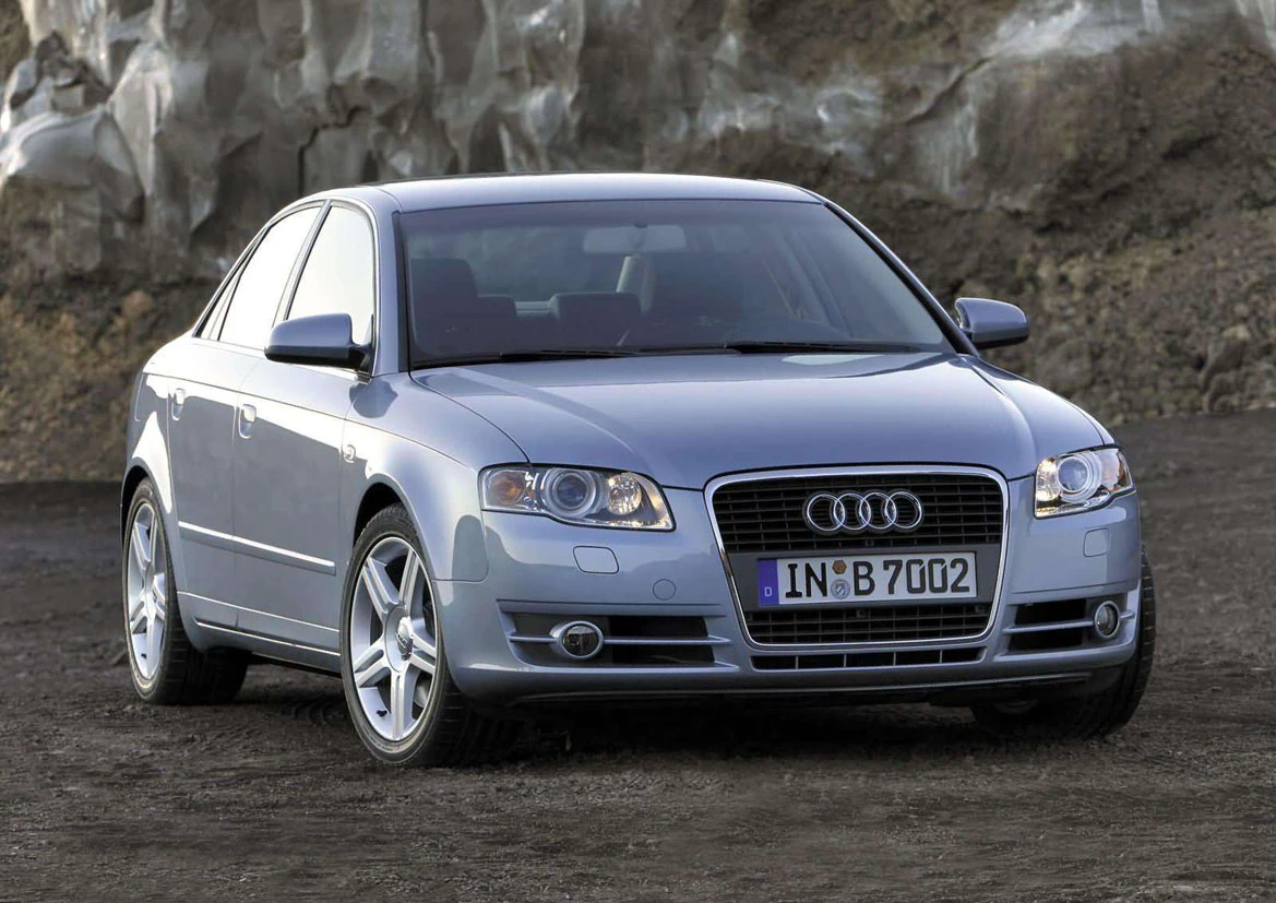 Silberner Audi A4 Limousine auf unbefestigtem Gelände vor einer Felswand, von vorne fotografiert.