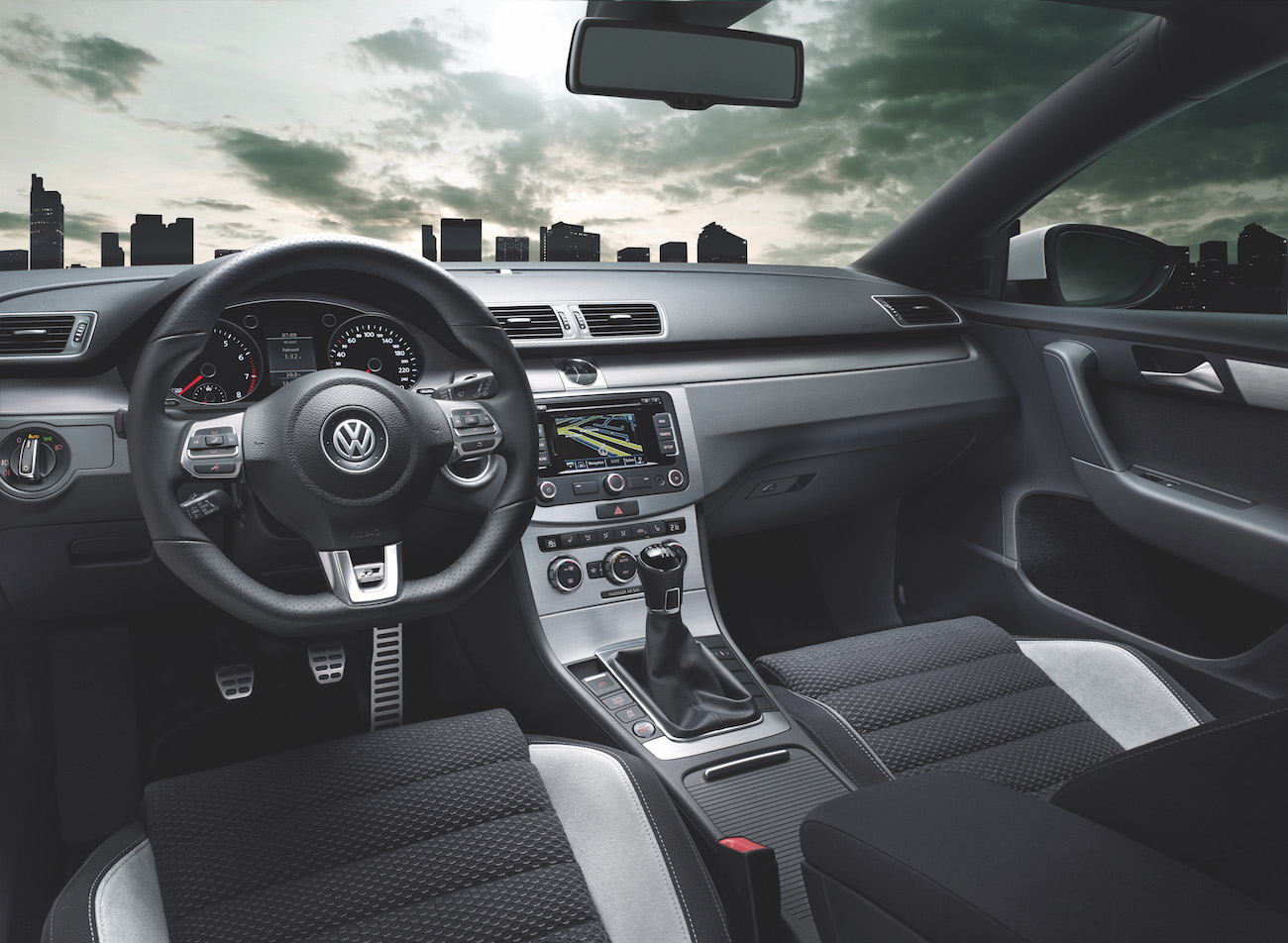 Innenraum eines modernen Autos mit Volkswagen-Emblem auf dem Lenkrad, Navigationssystem auf Mittelkonsole und Blick auf eine Stadt im Hintergrund.