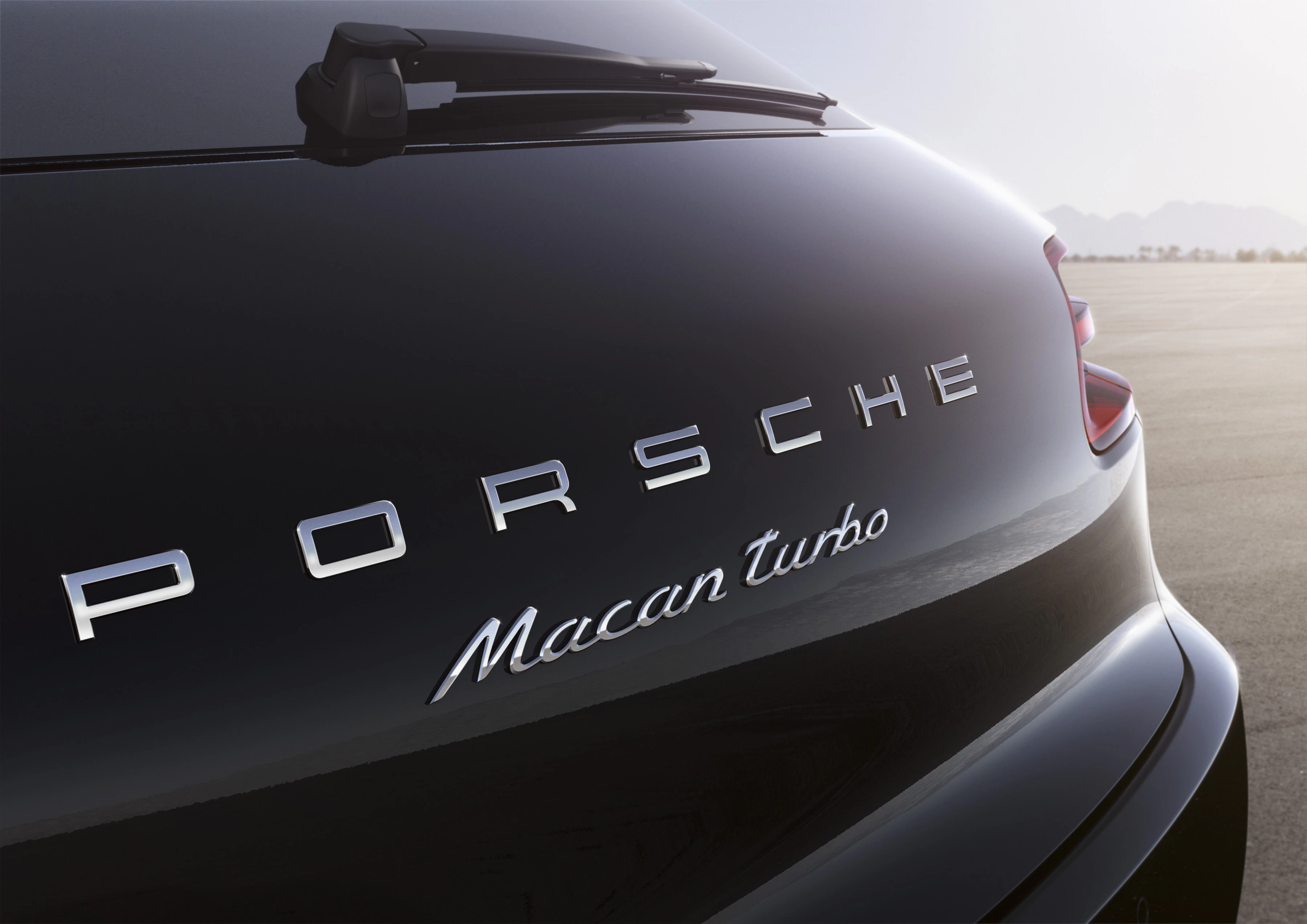 Rückansicht eines schwarzen Porsche Macan Turbo auf einer leeren Straße bei Tageslicht. Modellname und Marke sind deutlich sichtbar.
