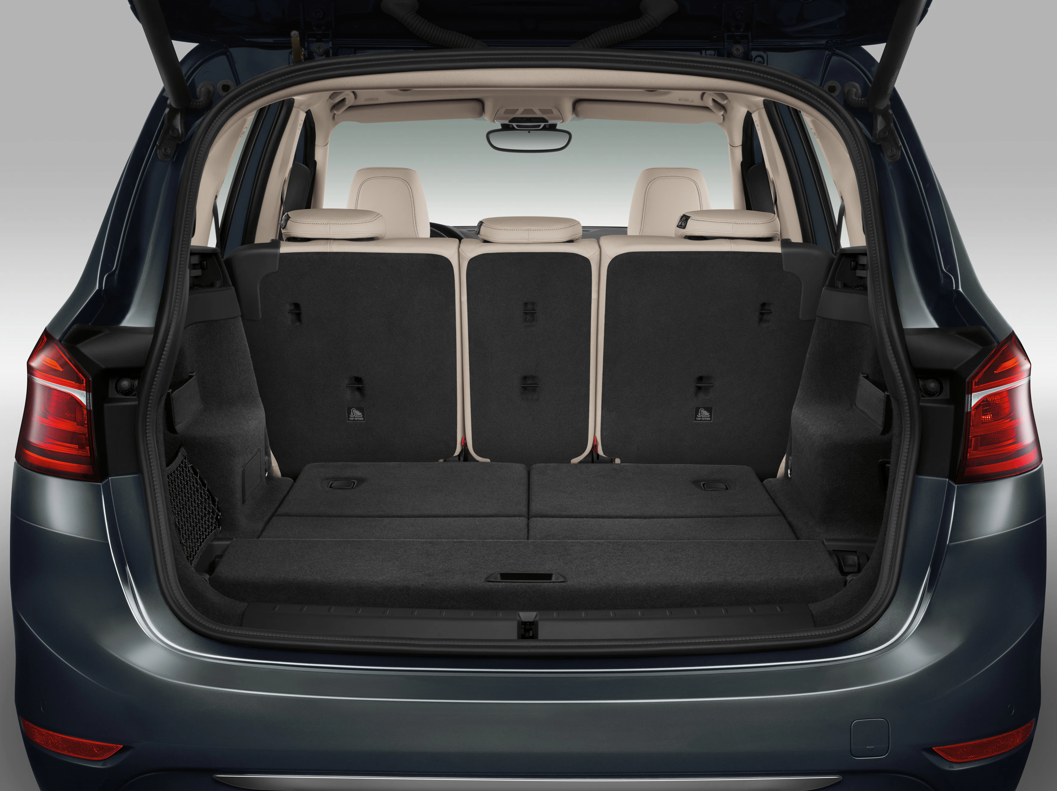 Innenraum eines Autos mit umgeklappter Rückbank, grauer Stoffbezug, beige Kopfstützen, zeigt geräumigen Kofferraum für mehr Stauraum.