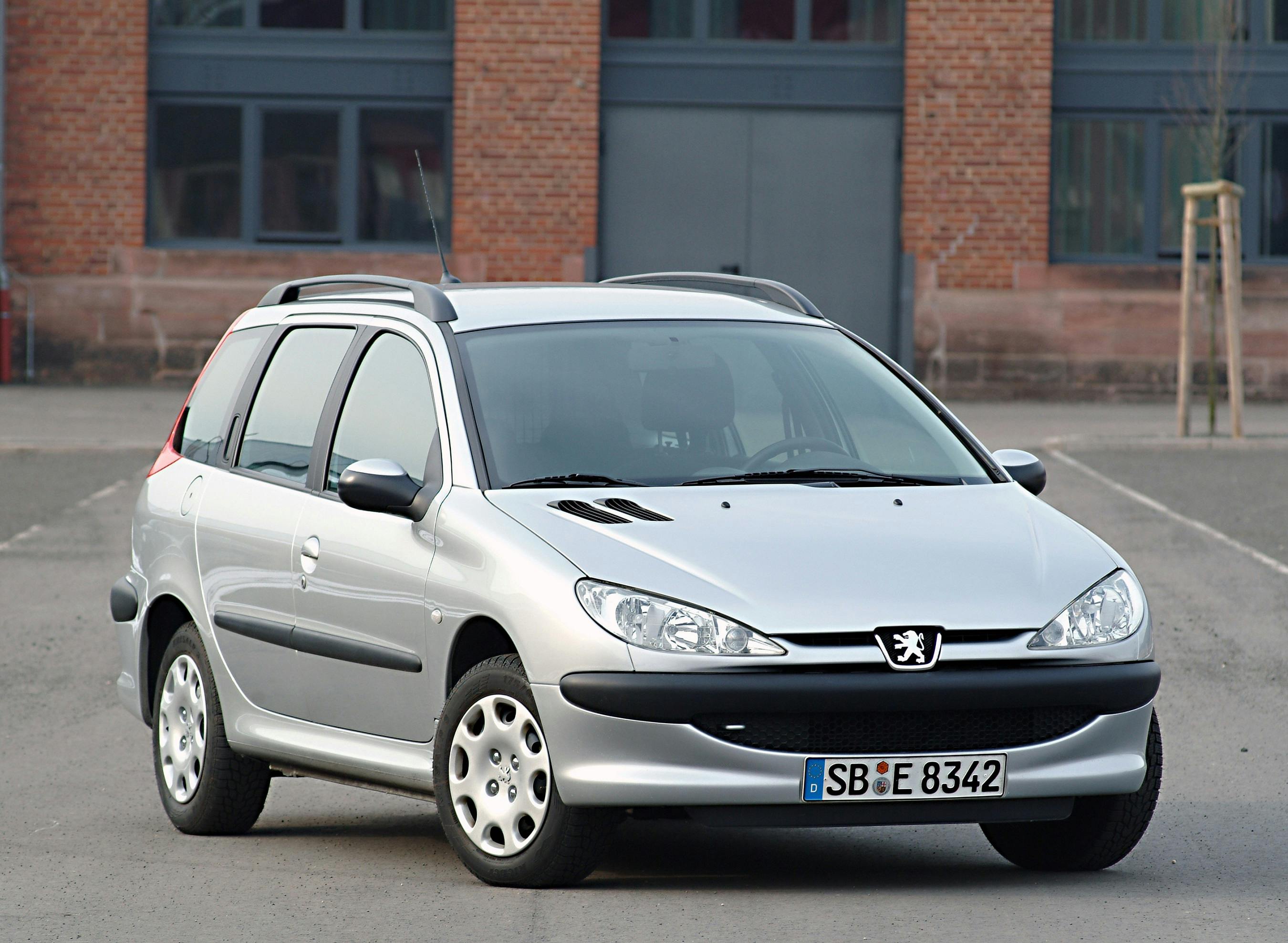 Silberner Peugeot 206 Kombi, geparkt auf grauem Asphalt vor einem Backsteingebäude mit Fenstern im Hintergrund.
