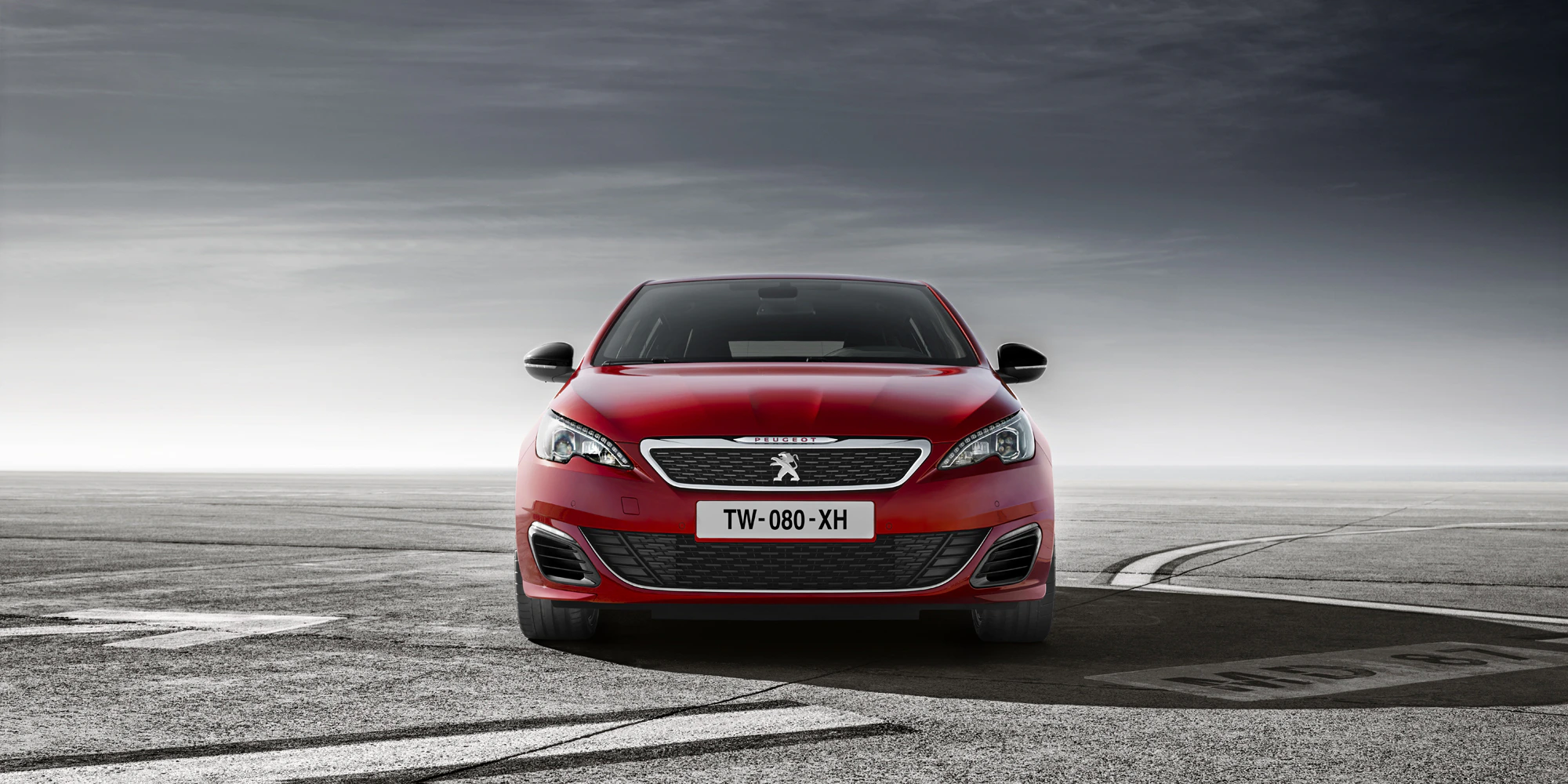 Roter Peugeot 308 auf einem leeren Asphaltplatz mit bewölktem Himmel im Hintergrund.