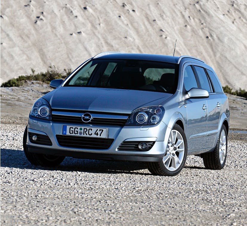 Silberner Kombi parkt auf einer Kiesfläche vor einem steinigen Hügel bei sonnigem Wetter.