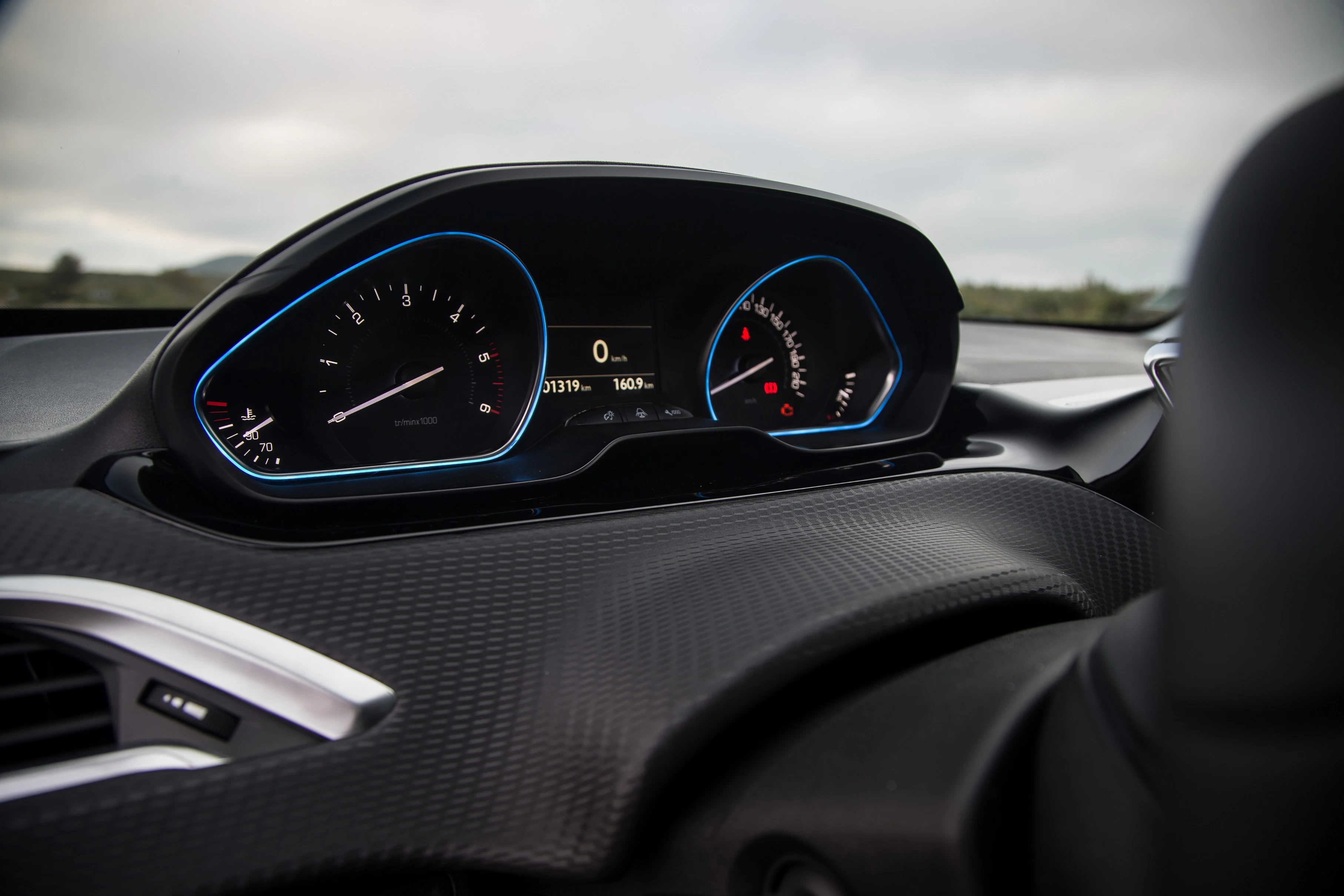 Nahaufnahme eines modernen Auto-Armaturenbretts mit analogem Tachometer und Drehzahlmesser sowie digitaler Anzeige.