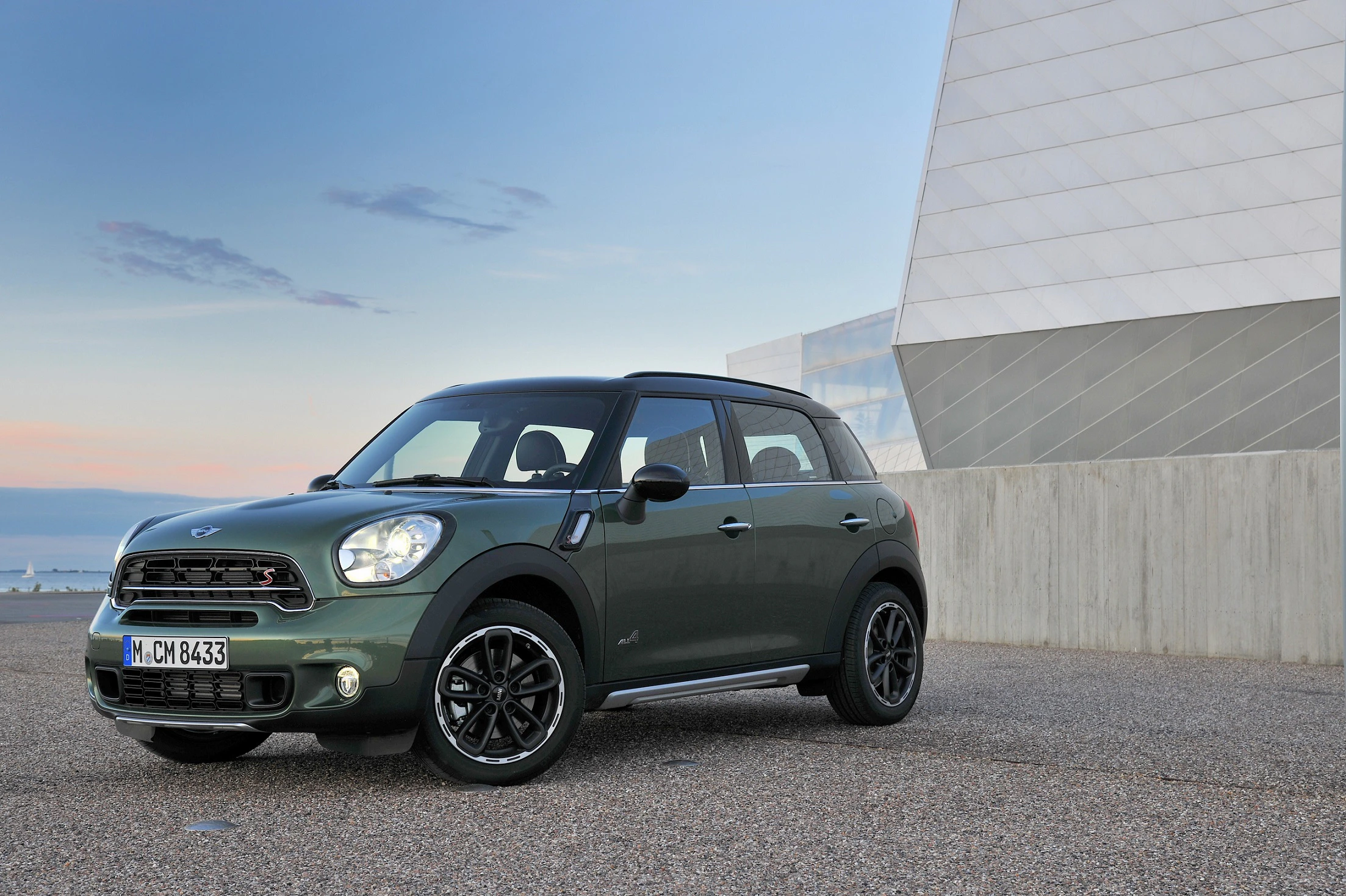 Grüner Mini Cooper SUV steht auf einem Parkplatz vor einem modernen Gebäude bei Sonnenuntergang.