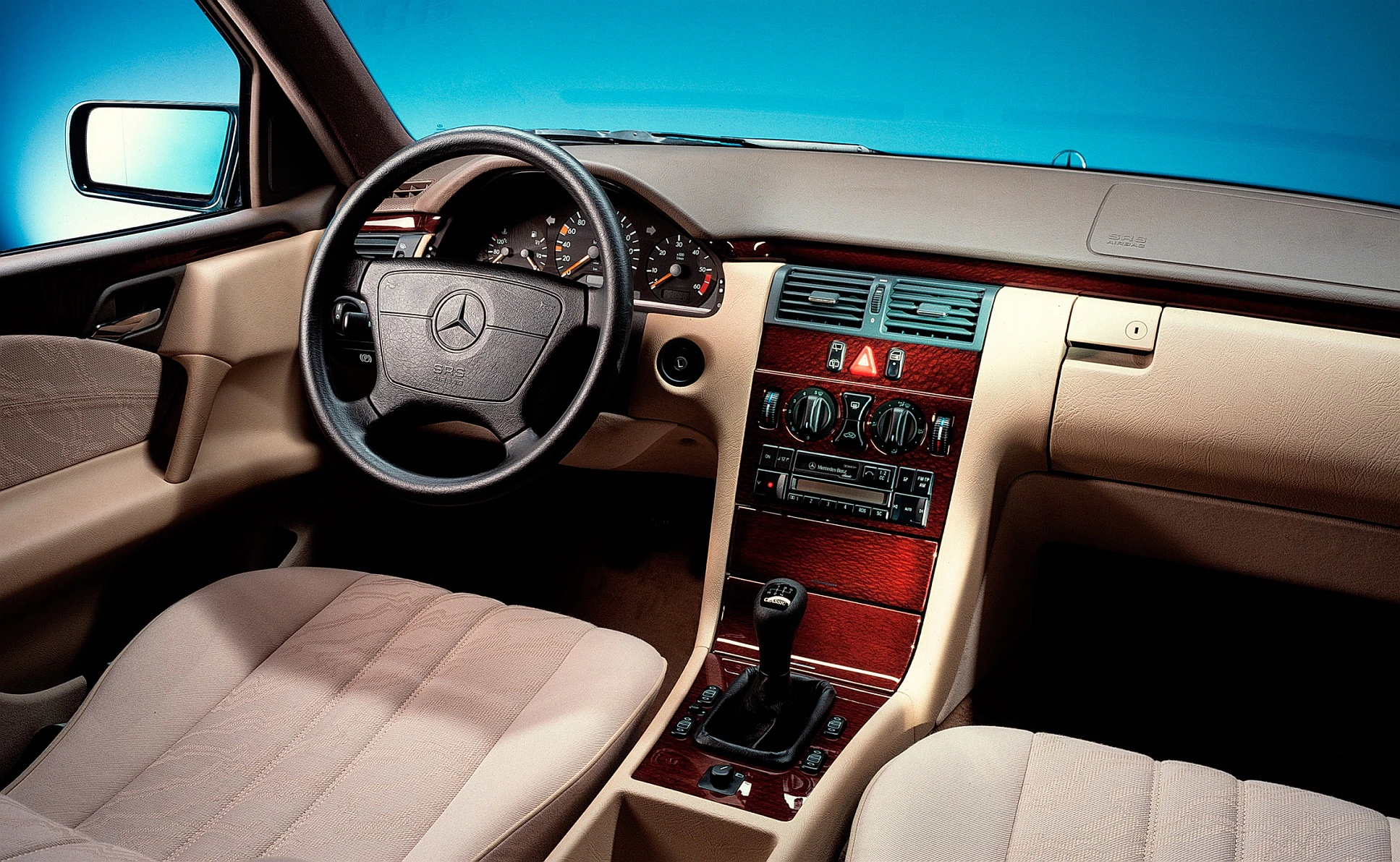 Innenraum eines Mercedes-Benz mit beigefarbenen Ledersitzen, hölzernen Details und einem traditionellen Armaturenbrettdesign.
