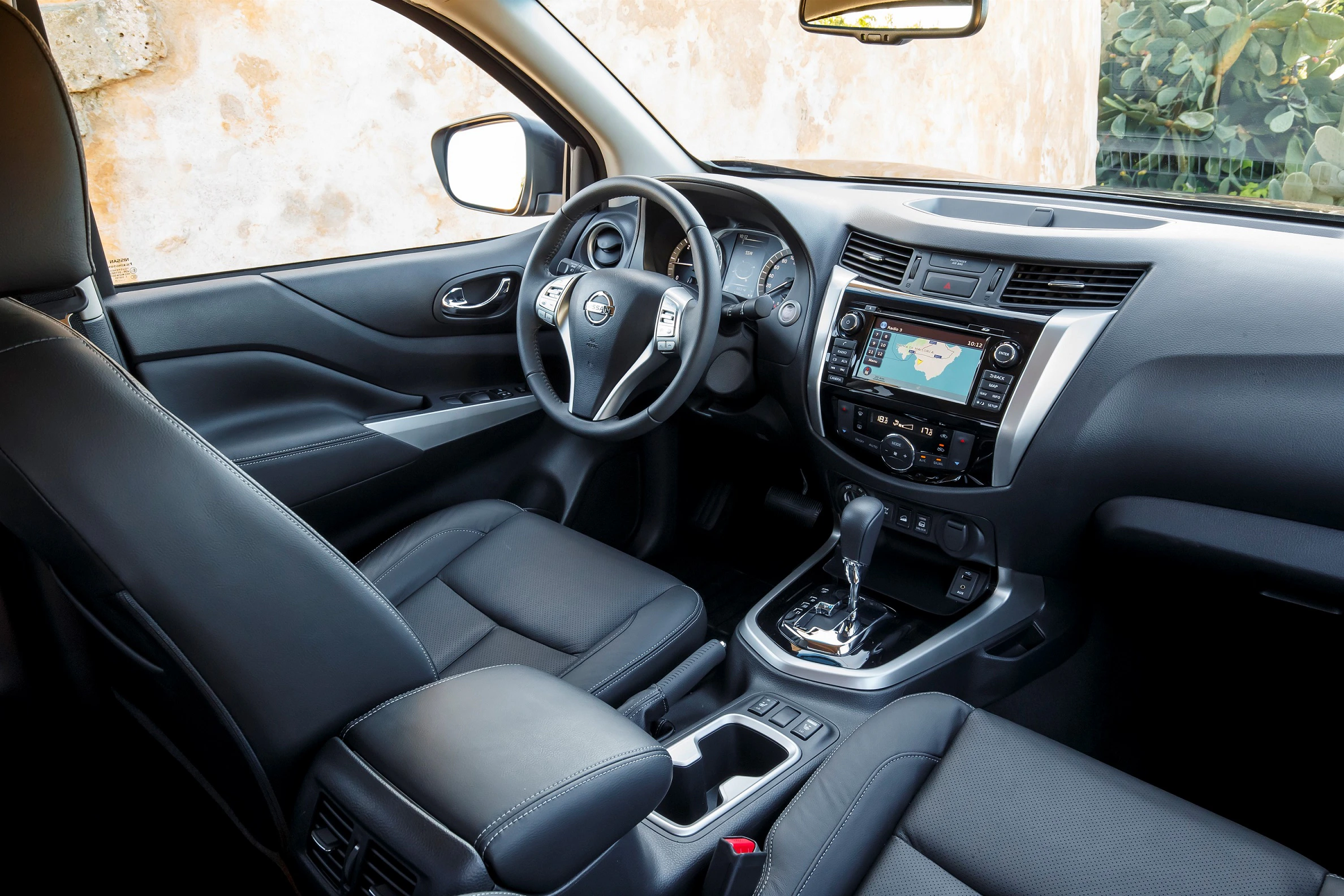 Innenraum eines modernen Autos mit Lederpolstern, Lenkrad, Mittelkonsole mit Bildschirm und Schalthebel, Tageslicht beleuchtet.