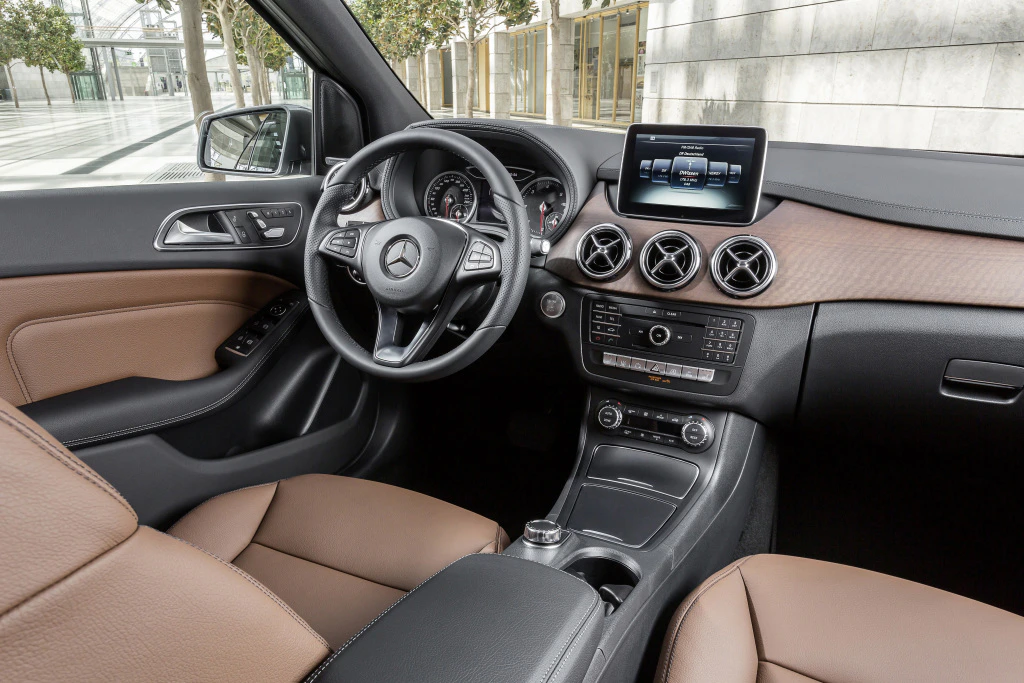 Innenraum eines modernen Mercedes-Benz mit braunen Ledersitzen, zentralem Display, multifunktionalem Lenkrad und stilvollem Armaturenbrett.