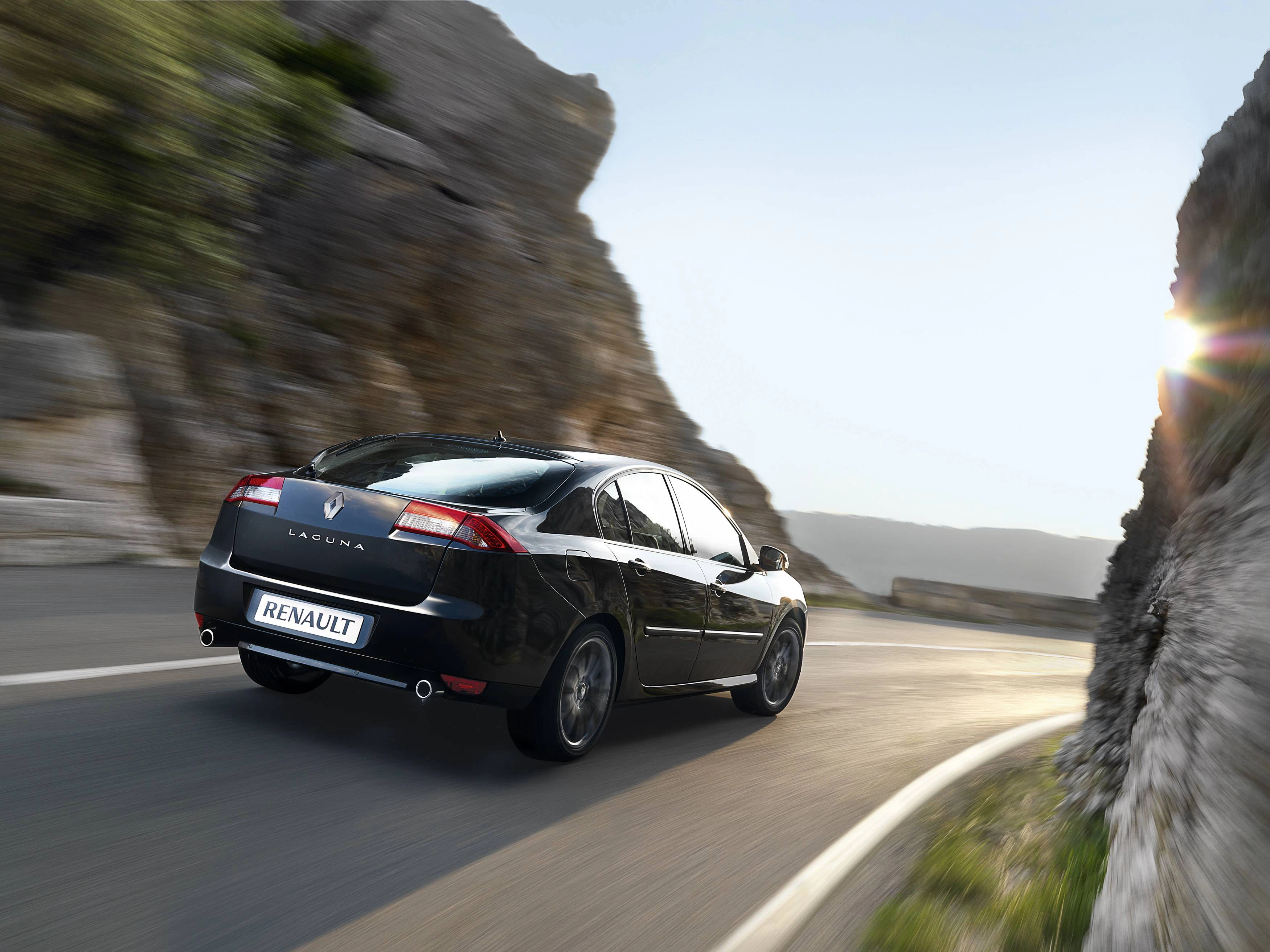 Schwarzer Renault Laguna fährt auf einer kurvenreichen Bergstraße bei Sonnenschein, umgeben von Felsen und blauem Himmel.