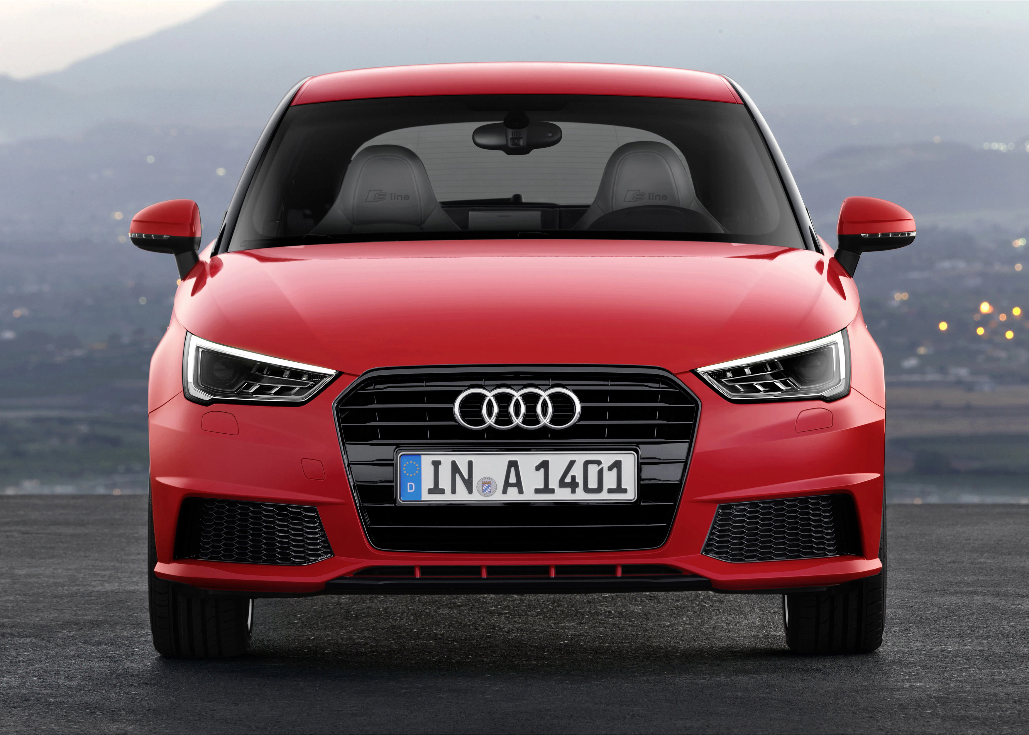 Roter Audi A1 von vorne auf einer Straße, Nummernschild sichtbar, verschwommene Landschaft im Hintergrund.
