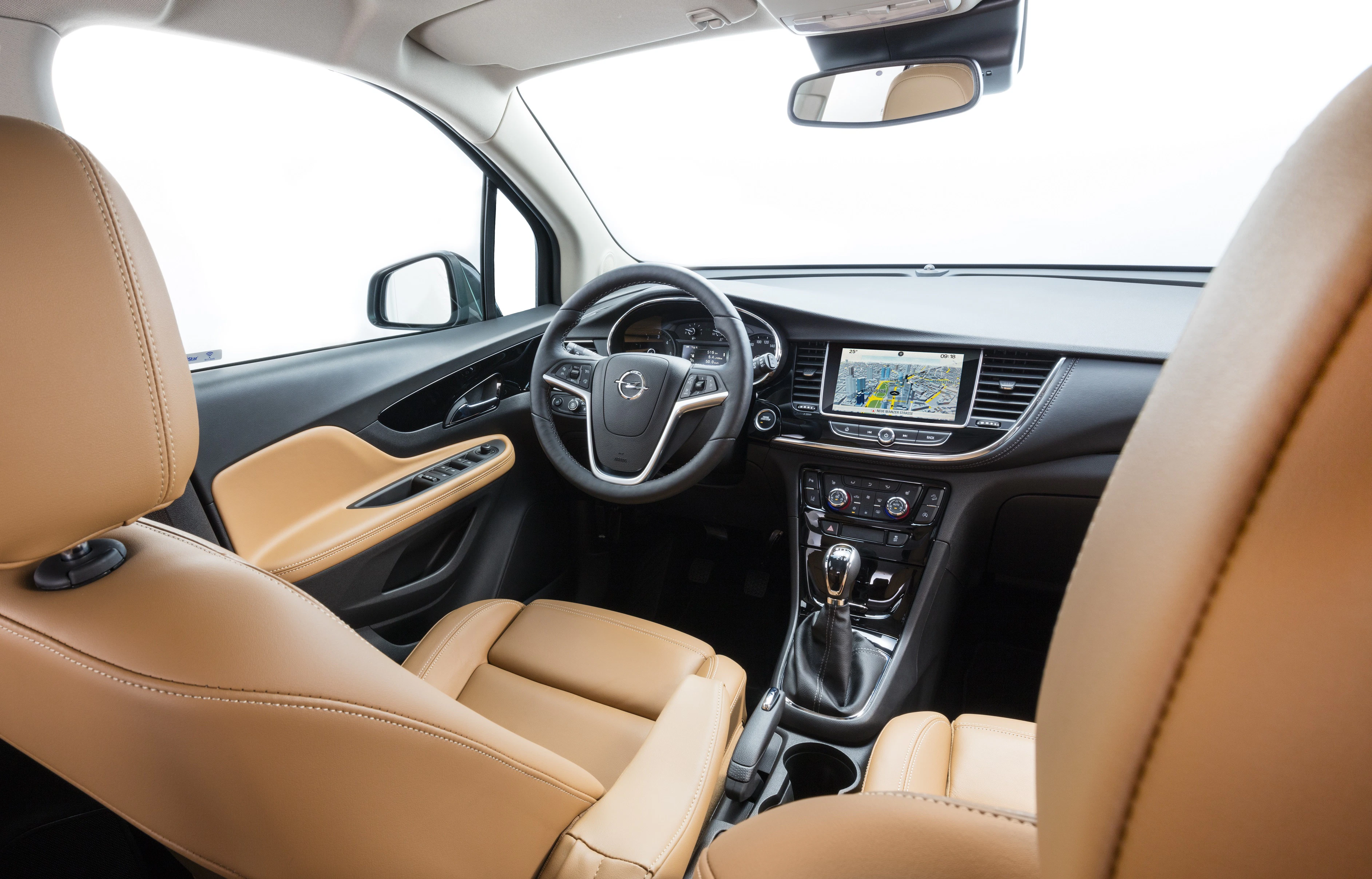 Innenraum eines Autos mit beigen Ledersitzen, Lenkrad und zentralem Display mit Navigationssystem; Blick vom Rücksitz aus.