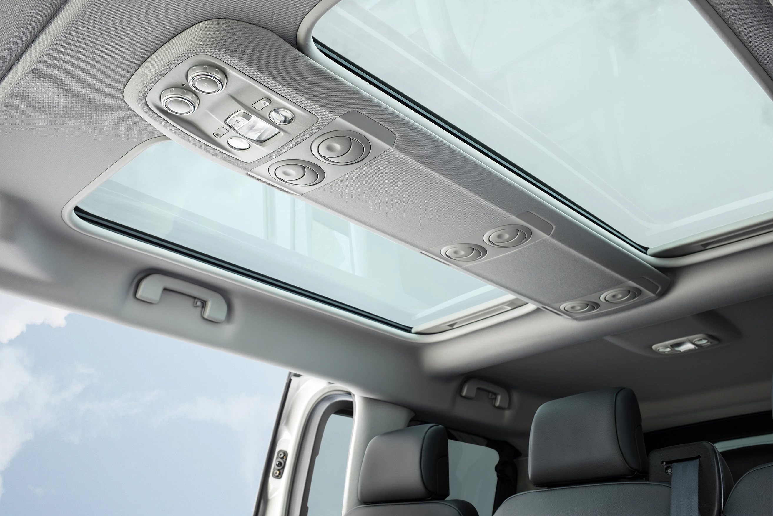 Innenansicht eines Autos mit geöffnetem Panoramadach und grauen Ledersitzen. Der Himmel ist durch das Glas sichtbar.