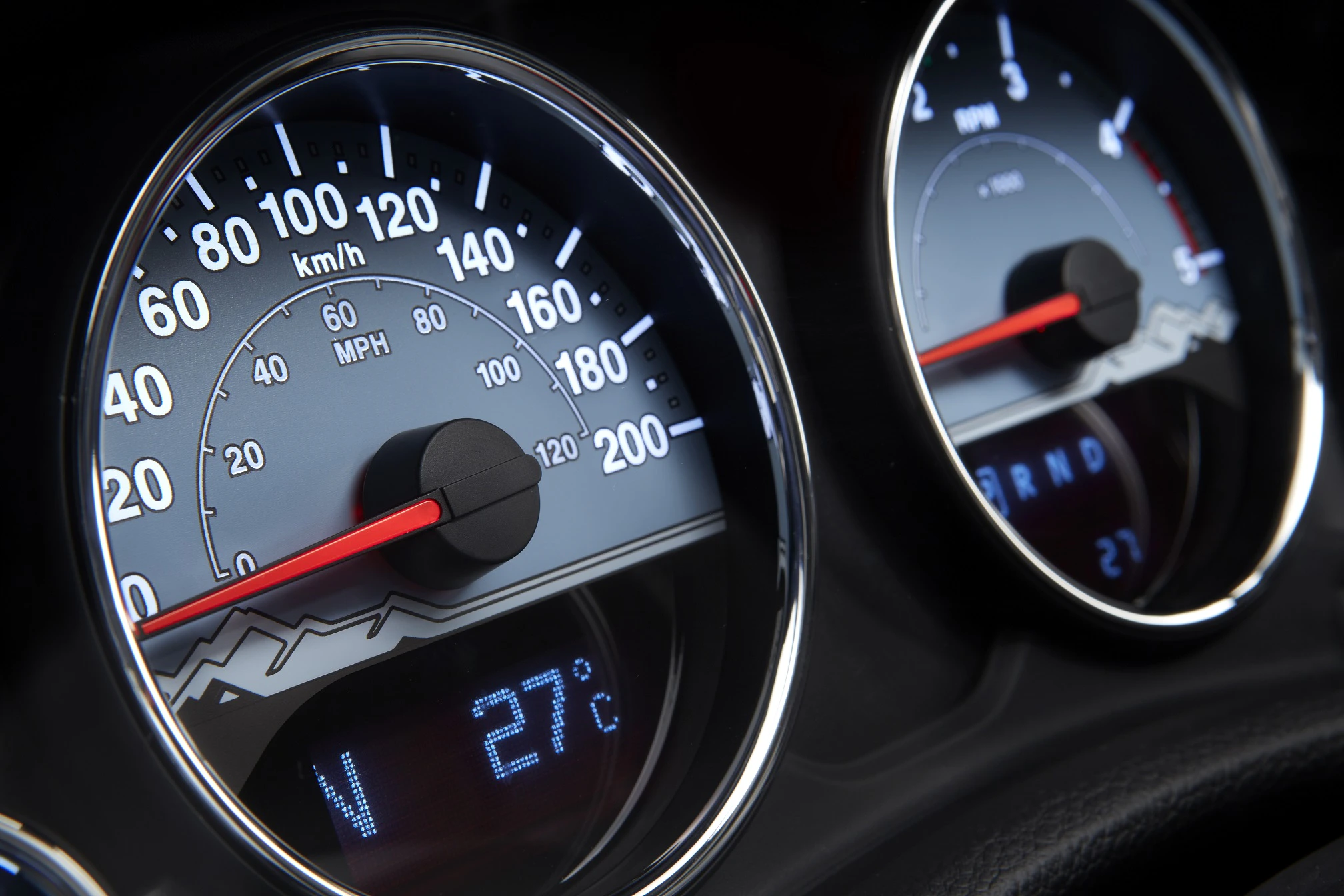 Nahaufnahme eines Autotachos mit Geschwindigkeitsanzeige in km/h und mph, sowie Temperaturanzeige von 27°C.
