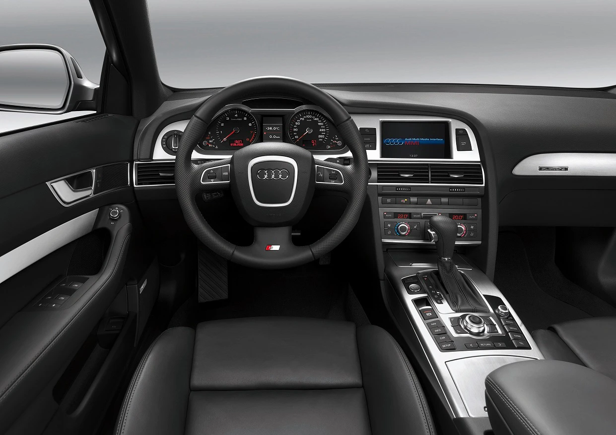 Innenraum eines Audi mit Lenkrad, Armaturenbrett, digitalen Anzeigen und Gangschaltung. Hochwertige schwarze Ledersitze und elegantes Design.