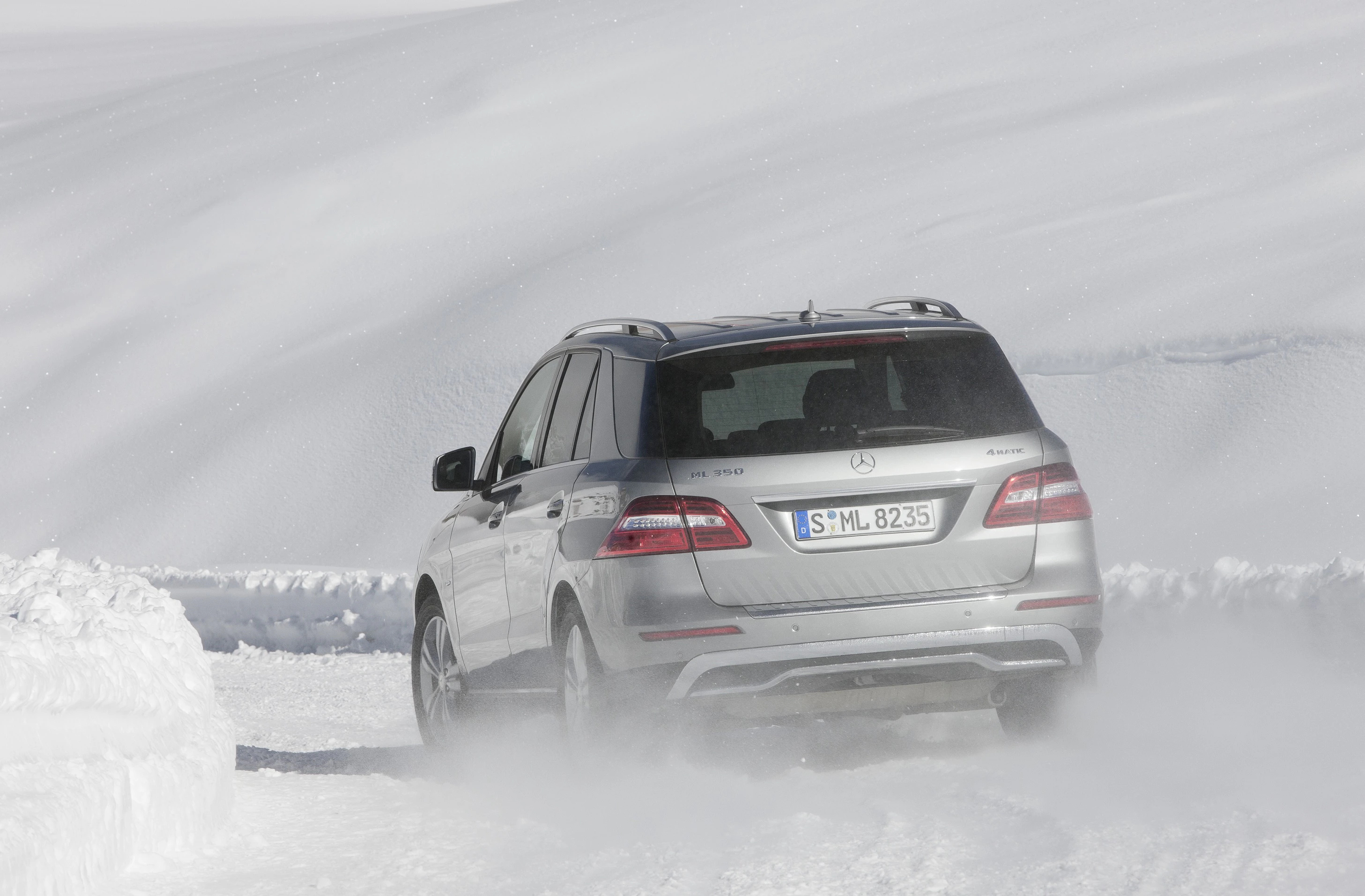 Ein silberner SUV fährt durch schneebedecktes Gelände, hinterlässt Spuren im Schnee. Die Umgebung ist mit Schnee bedeckt.