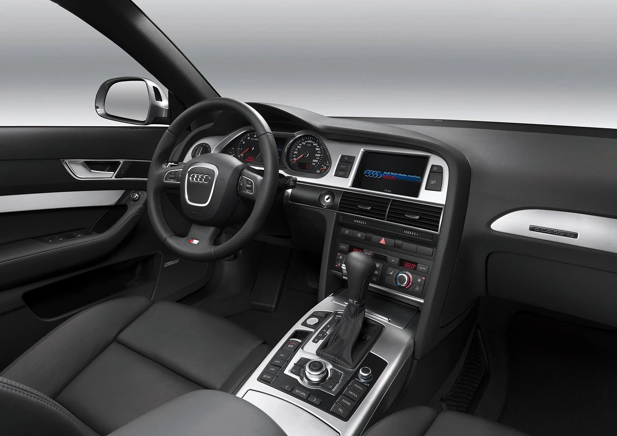 Innenraum eines Audi-Autos mit Lederlenkrad, Schaltknüppel, Touchscreen und modernen Instrumenten in einer eleganten, dunklen Farbgebung.