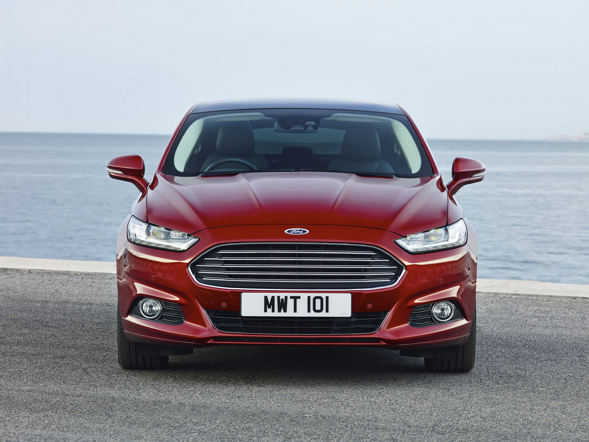 Roter Ford auf einer Straße vor dem Meer, betrachtet aus der Frontansicht. Nummernschild mit der Aufschrift "MWT 101".