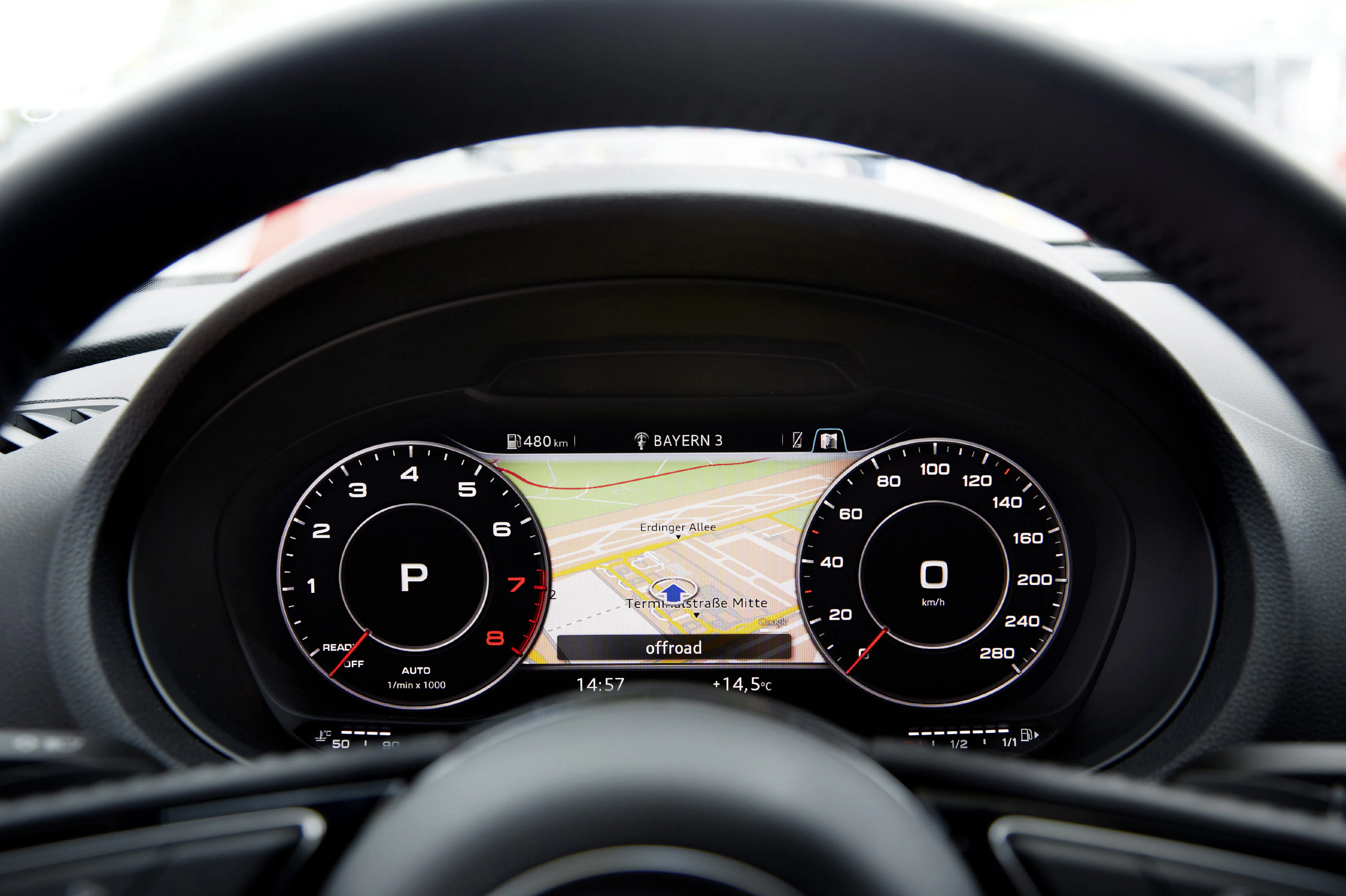 Digitales Armaturenbrett eines Autos, zeigt Navigationssystem, Geschwindigkeitsanzeige und Drehzahlmesser, bei Bayern 3 eingestellt.