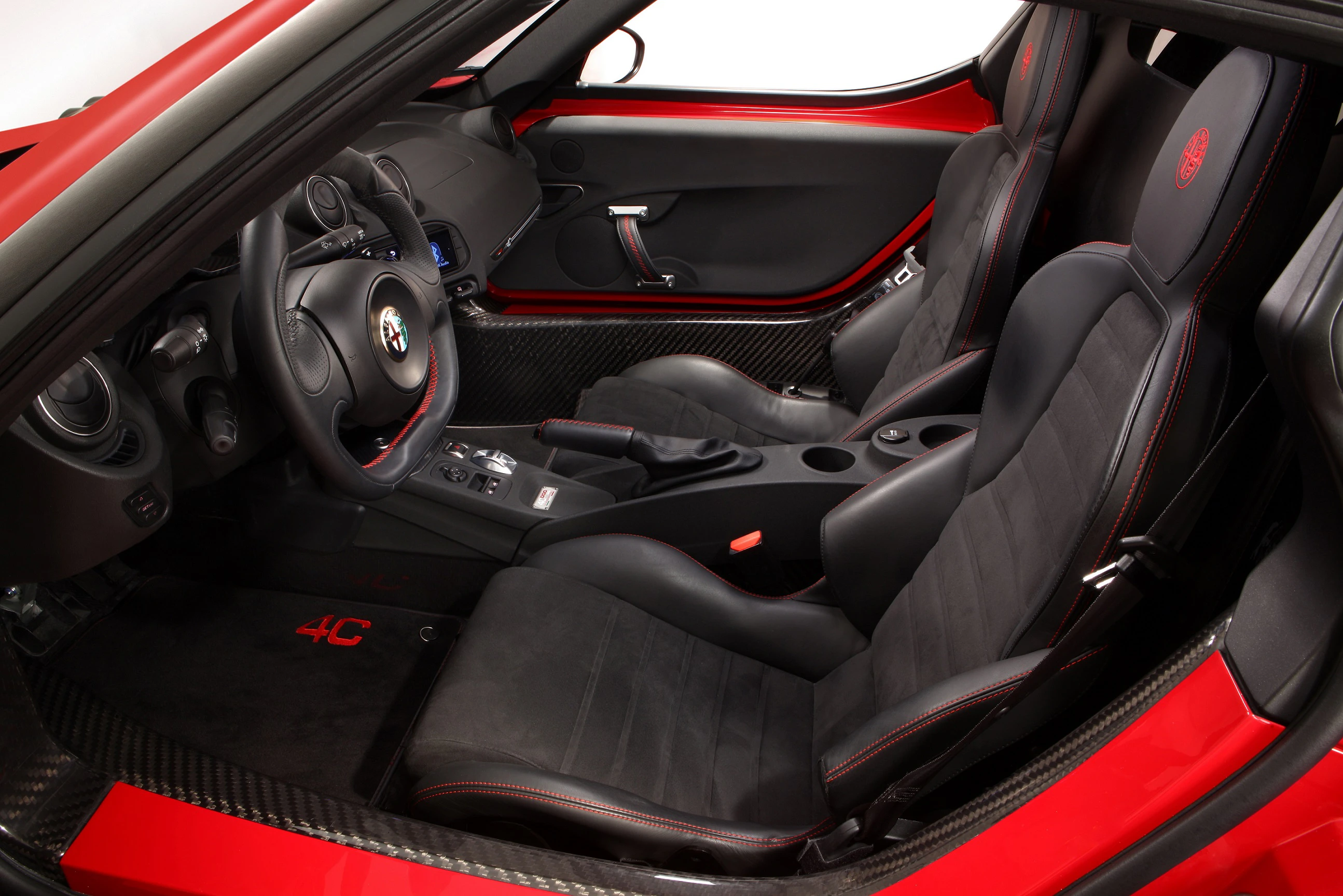 Innenraum eines sportlichen Autos mit schwarzem Lederinterieur und roten Ziernähten; Schalthebel in der Mitte, Sportlenkrad links.