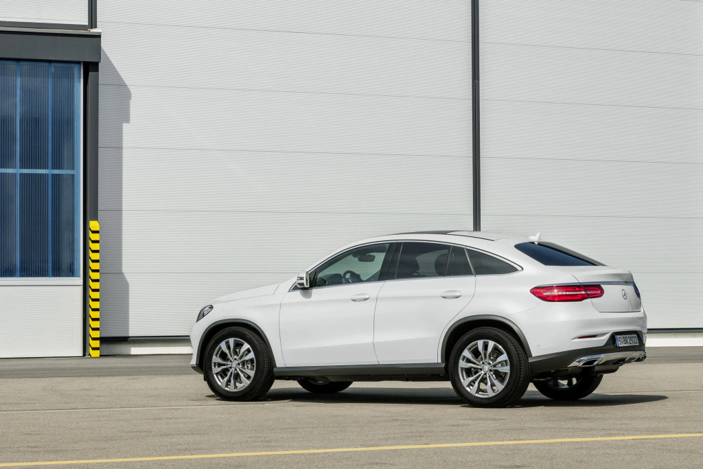 Weißer SUV geparkt vor einem modernen Industriegebäude mit grauen Wänden und blauen Fenstern auf asphaltierter Fläche.