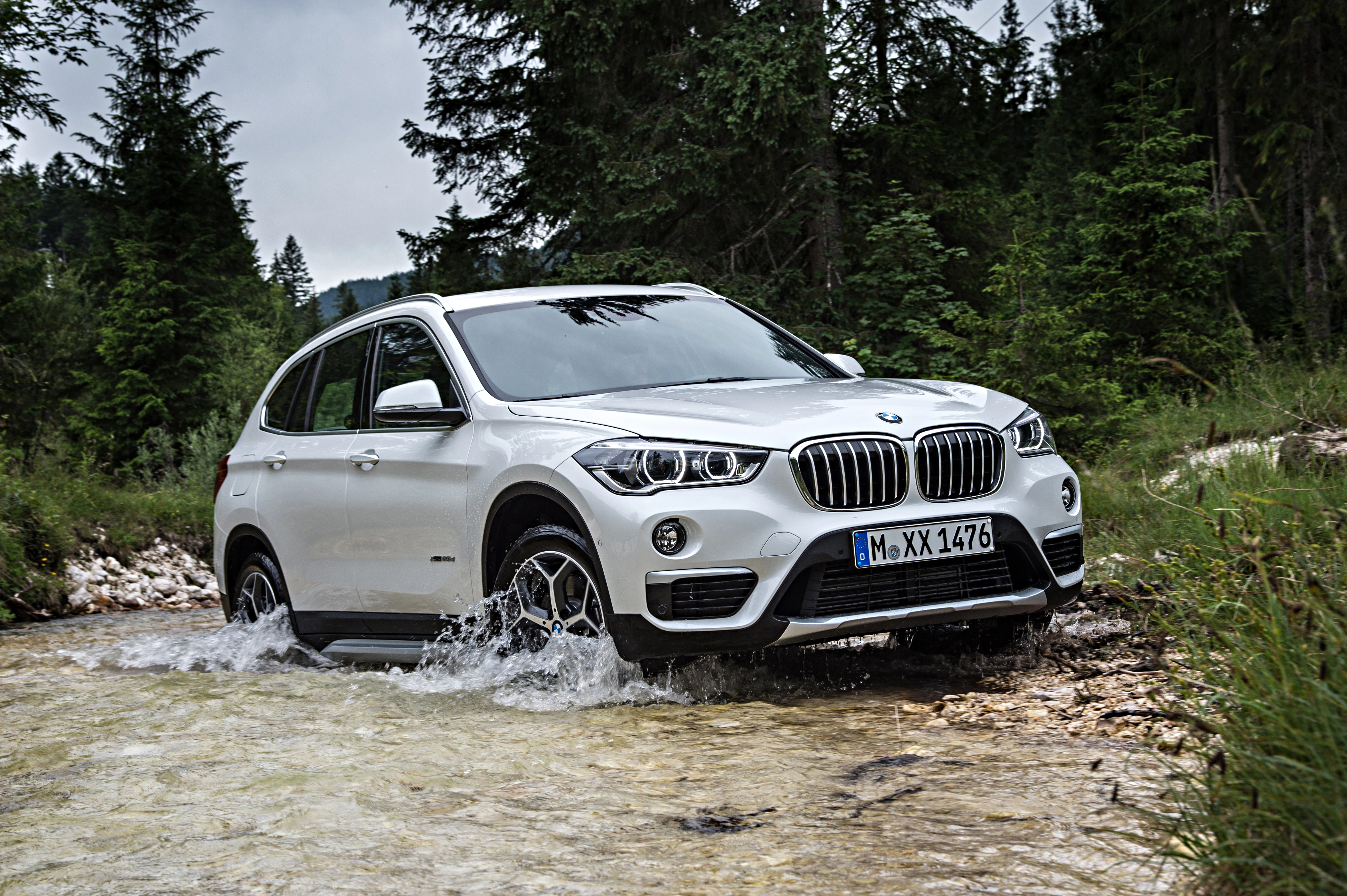 Ein weißer SUV durchquert einen flachen Bach in einer bewaldeten, grünen Umgebung.