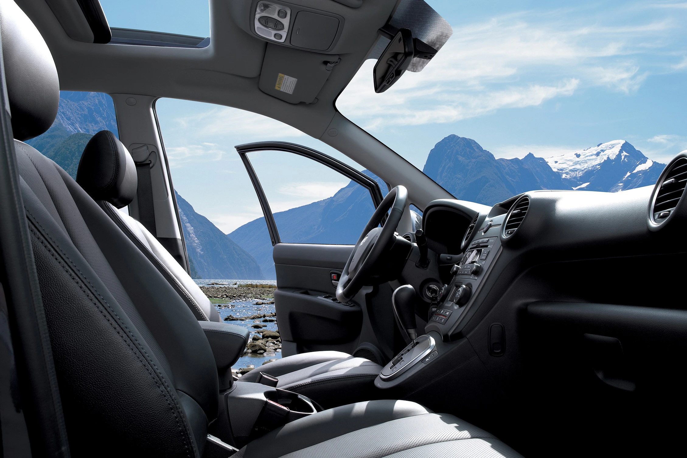 Innenraum eines Autos mit offenem Fahrerfenster vor einer malerischen Berglandschaft und blauem Himmel.