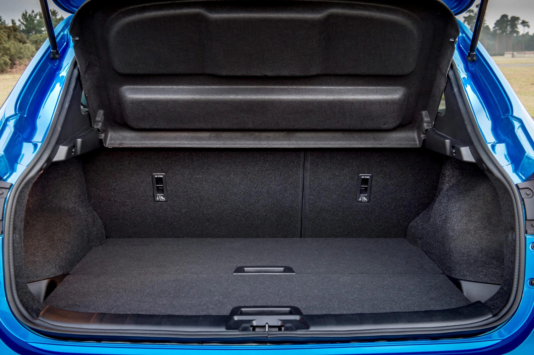 Geöffneter Kofferraum eines blauen Autos mit klappbaren Rücksitzen und schwarzem Innenraum auf einer draußen aufgenommenen Aufnahme.