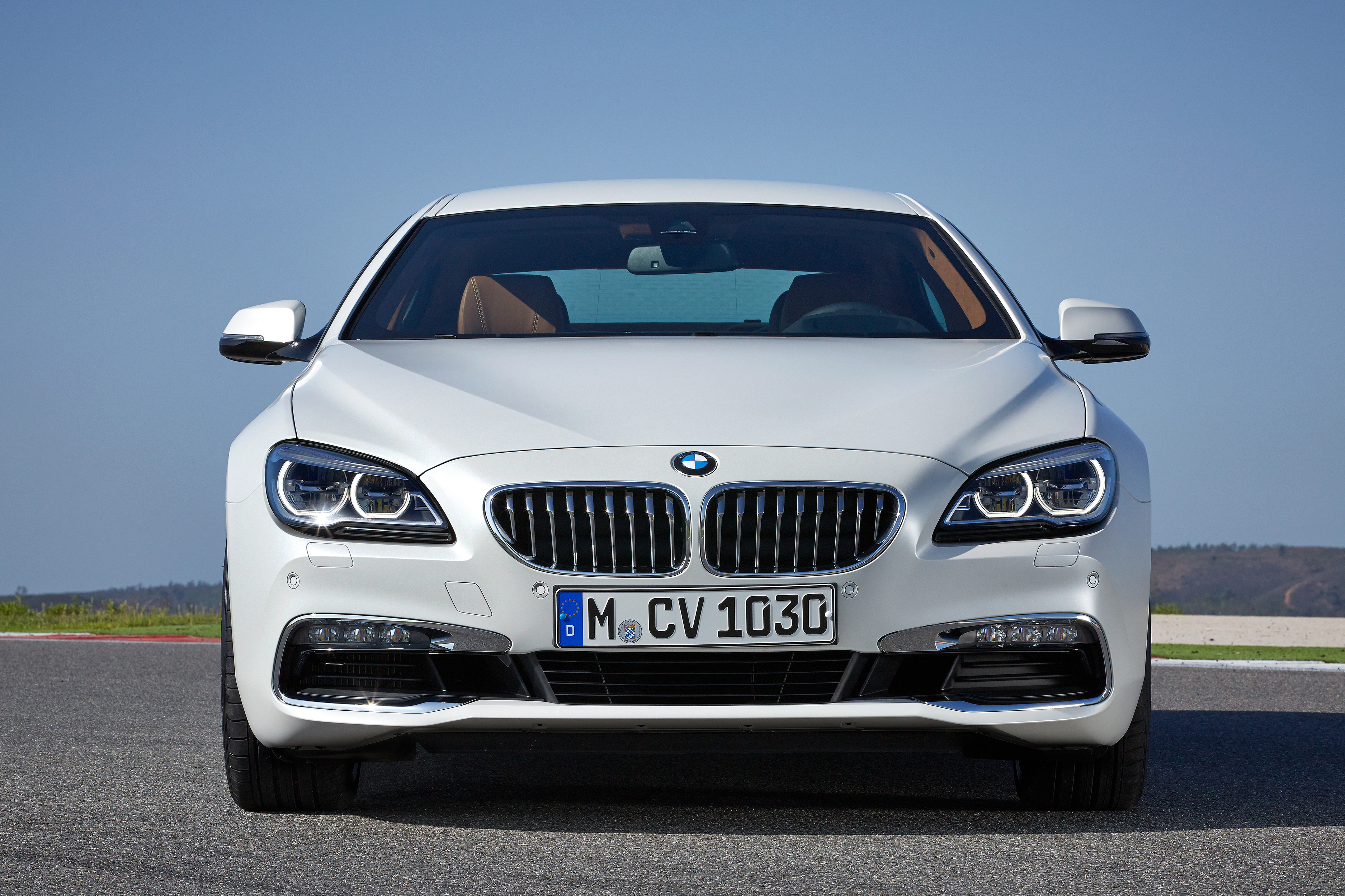 Weißer BMW auf einer Straße bei klarem Himmel, Frontansicht mit sichtbarem Kühlergrill und Scheinwerfern.