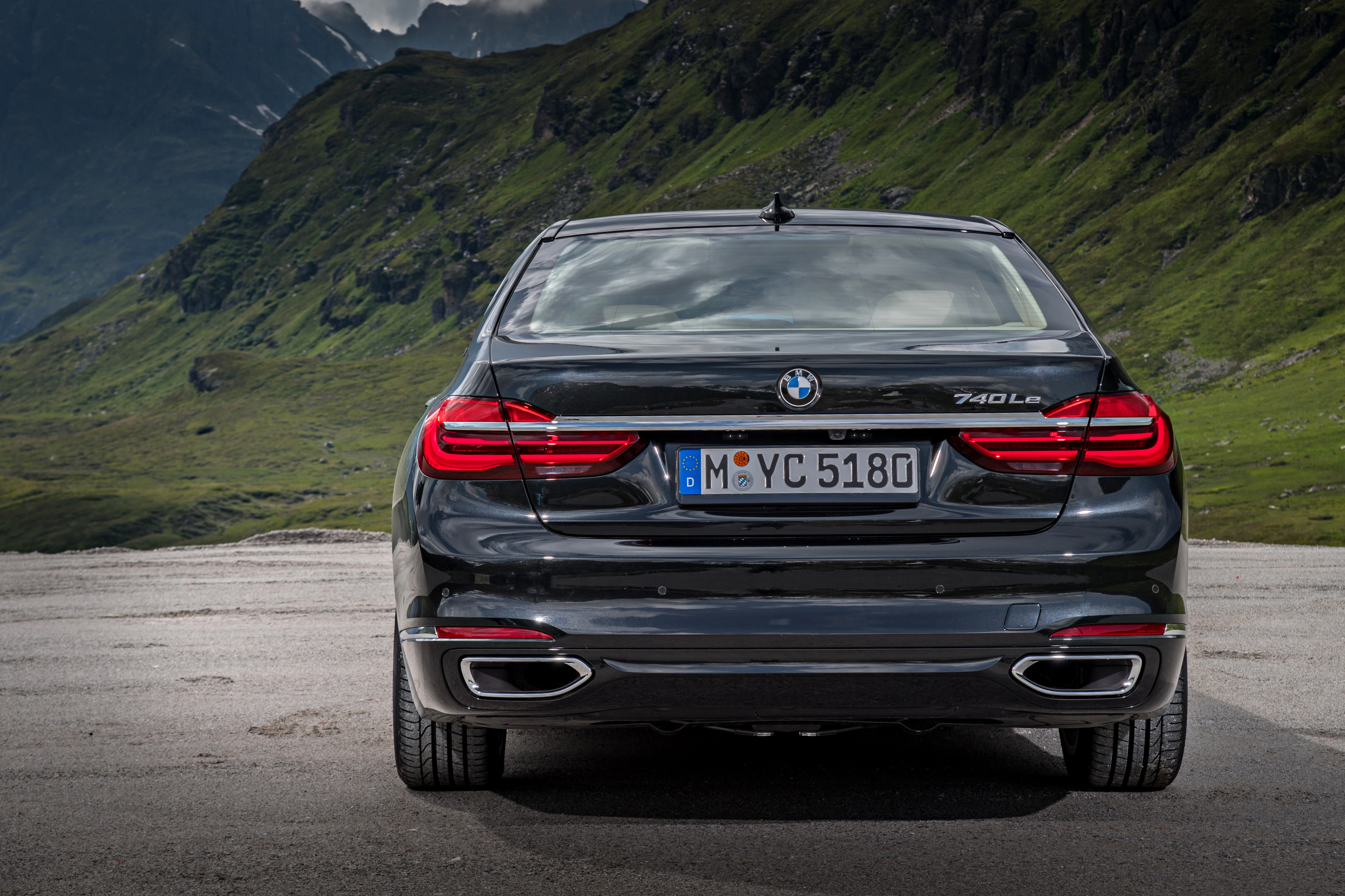 Heckansicht eines schwarzen BMW 740Le vor einer Berglandschaft, mit LED-Rückleuchten und sichtbaren Auspuffrohren.