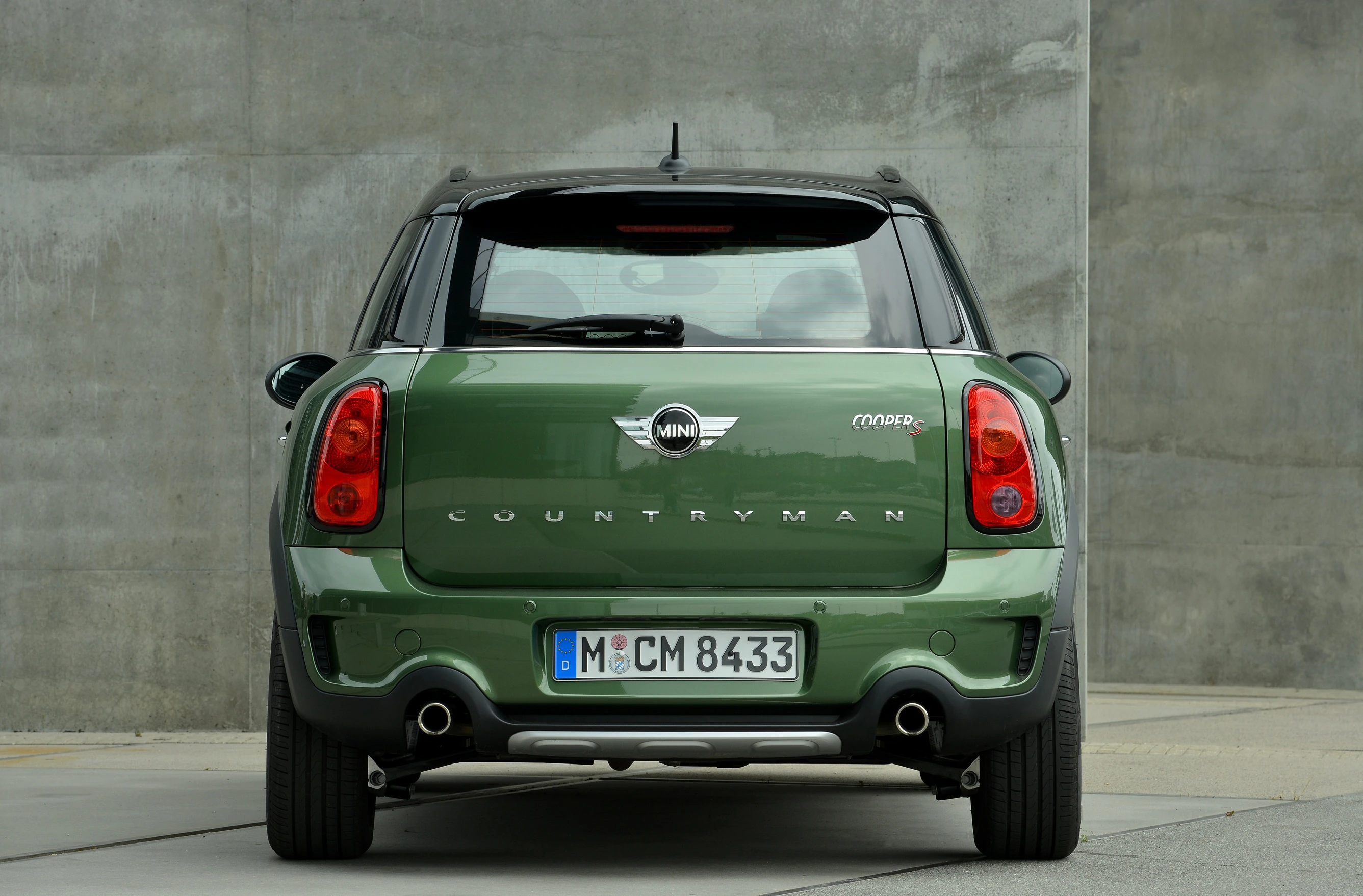 Grüner Mini Countryman aus der Rückansicht, stehend vor einer grauen Betonwand. Nummernschild mit Münchener Kennzeichnung sichtbar.