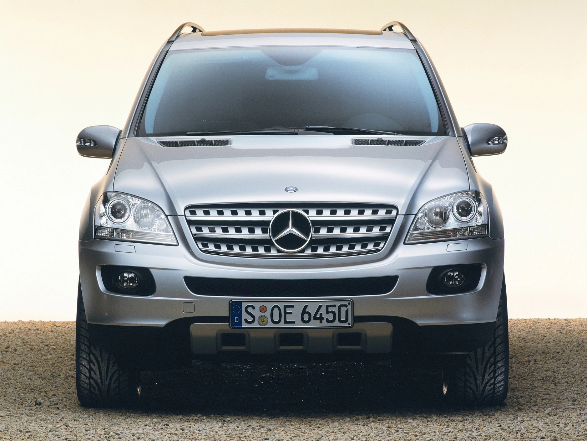 Silberner Mercedes-Benz SUV von vorne, auf Kies stehend, mit sichtbarem Emblem und Kennzeichen.