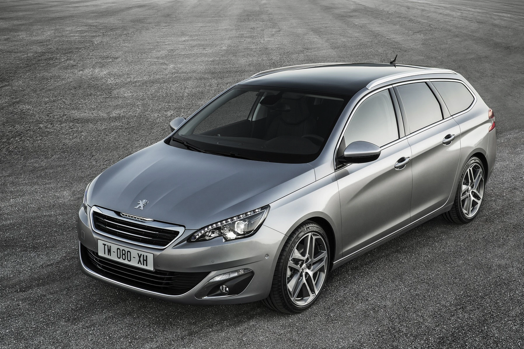Silberner Peugeot 308 SW parkt auf grauem Asphalt. Elegantes, modernes Design mit schwarzen Fenstern und markanten Felgen.
