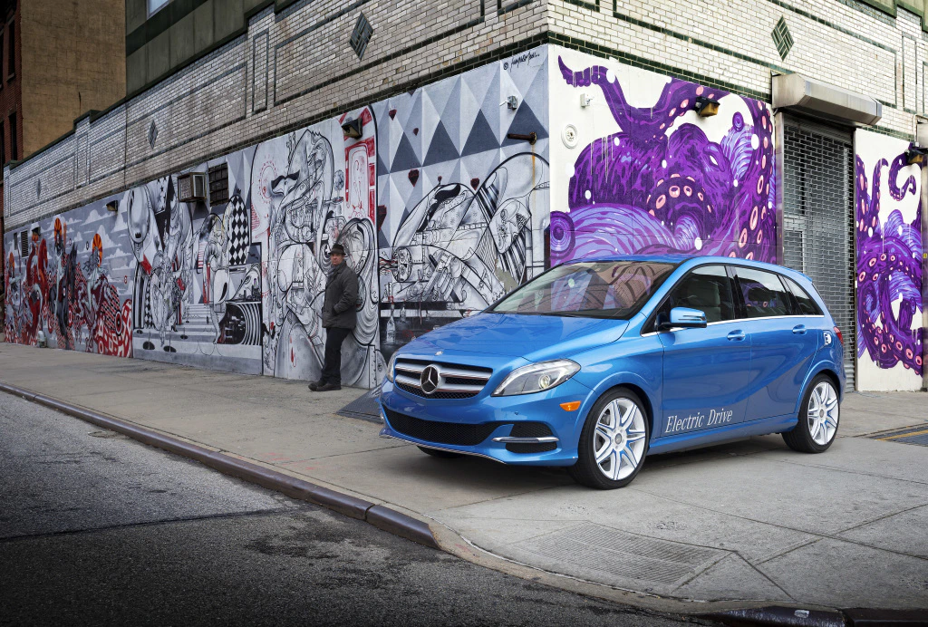 Blaues Elektroauto von Mercedes-Benz parkt vor einer Wand mit auffälligem Graffiti in einer städtischen Umgebung.