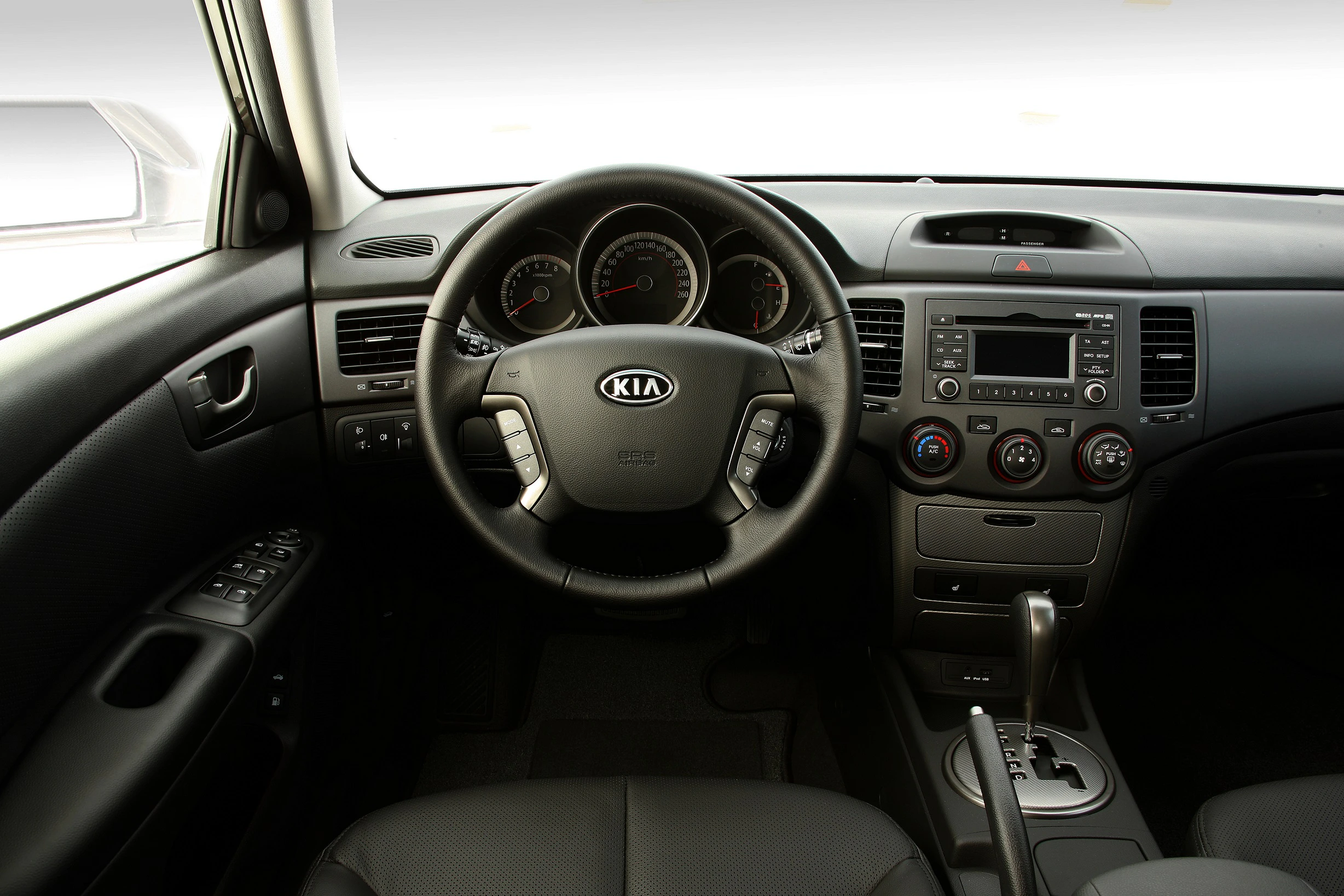 Innenraum eines Autos mit Kia-Logo auf dem Lenkrad, Armaturenbrett mit Tacho und Mittelkonsole mit Radio und Klimaanlage.