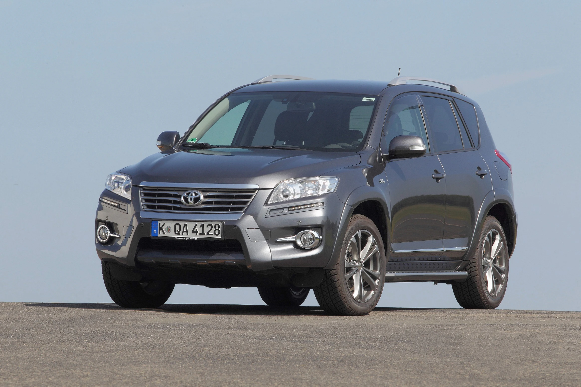 Grauer Toyota-SUV steht auf Asphalt vor blauem Himmel. Frontalansicht mit Scheinwerfern und markantem Kühlergrill.