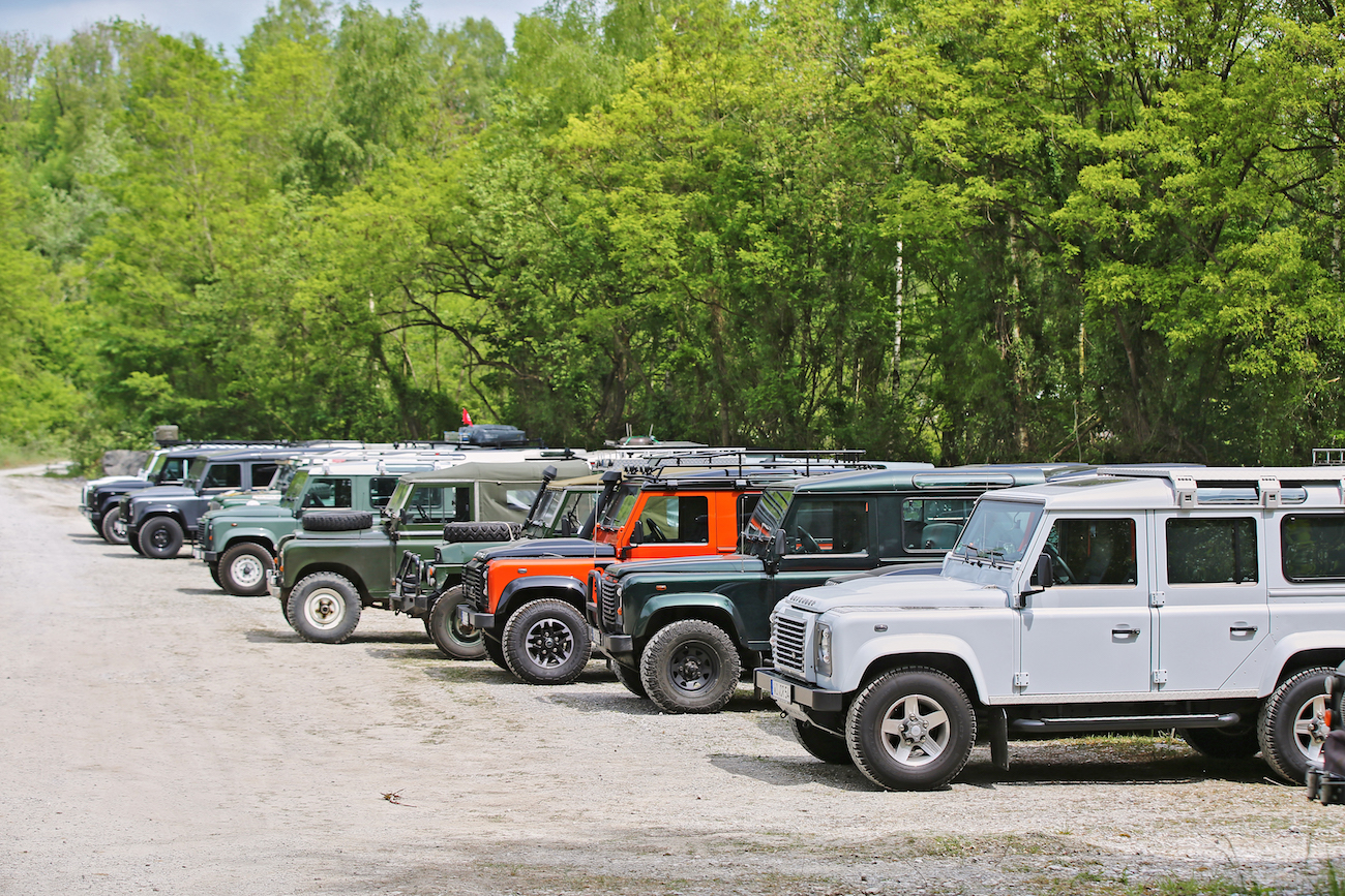 Eine Reihe von Geländewagen parkt auf einem Schotterweg, umgeben von grünen Bäumen im Hintergrund.