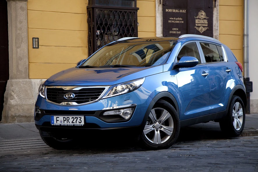 Blauer Kia SUV geparkt auf einer Kopfsteinpflasterstraße vor einem historischen Gebäude.