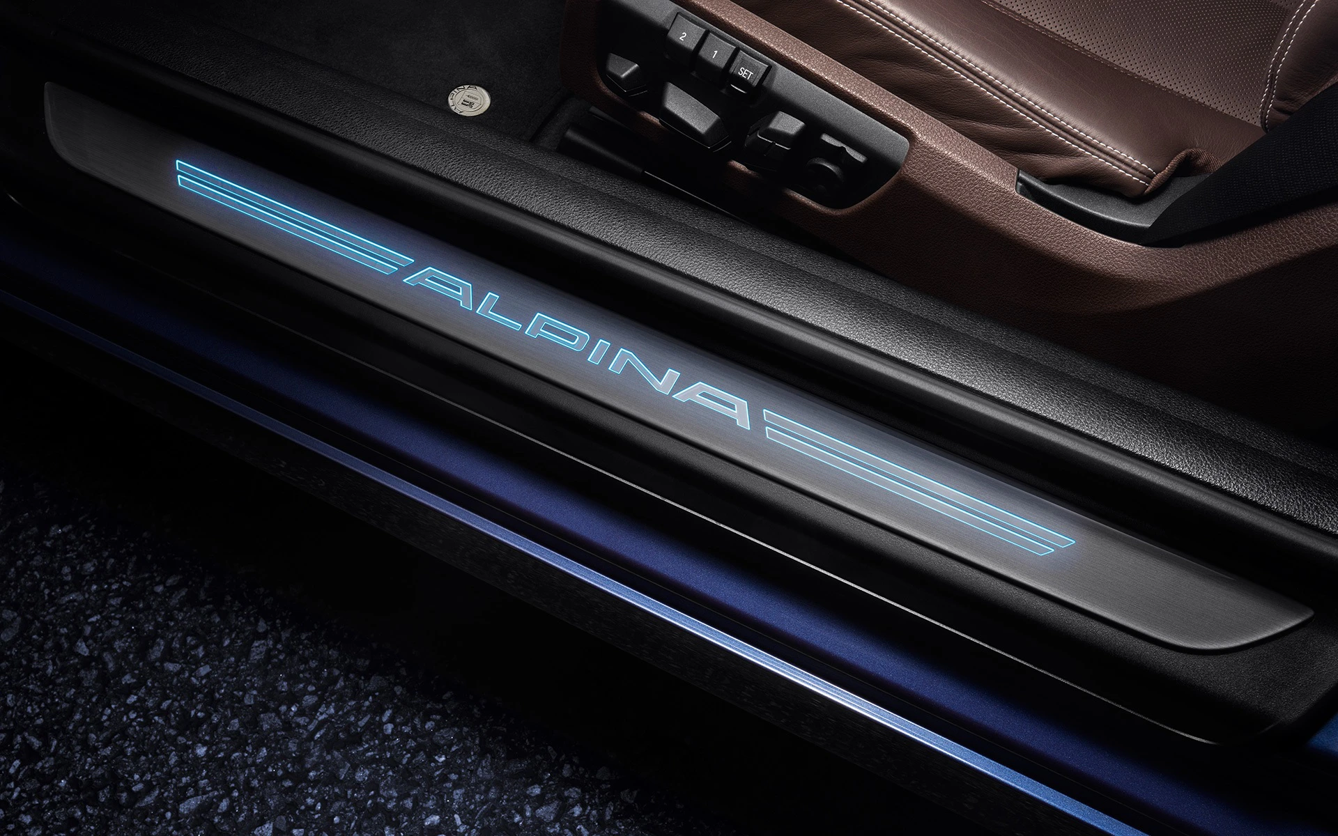 Beleuchteter Türschweller eines Autos mit dem Schriftzug "ALPINA" in blauem Licht. Dunkler Innenraum mit braunem Sitz.