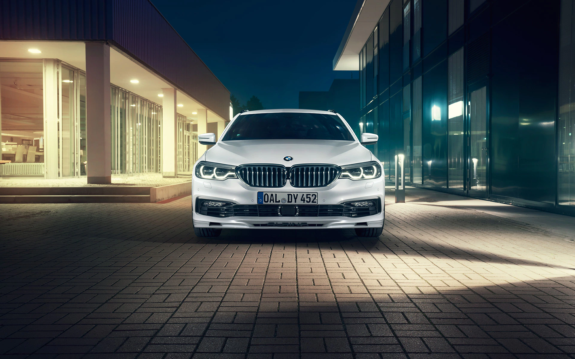 Weißer BMW in einem modernen, beleuchteten Stadtviertel, frontal fotografiert bei Nacht.