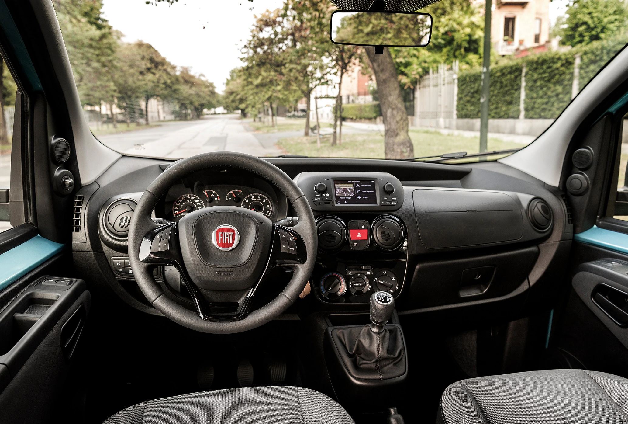 Innenraum eines Autos mit Fiat-Logo auf dem Lenkrad, Armaturenbrett mit Anzeigen und Schalthebel. Blick durch die Windschutzscheibe auf eine Straße.