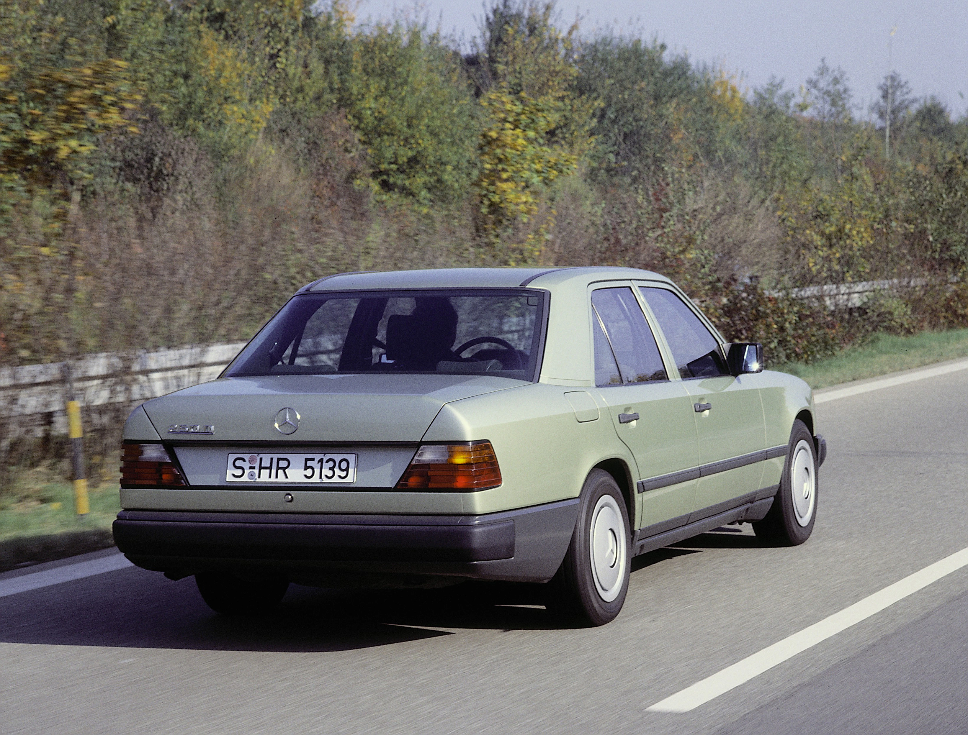 Ein grauer Mercedes-Benz E-Klasse fährt auf einer Landstraße, umgeben von Bäumen und einem Schutzzaun.