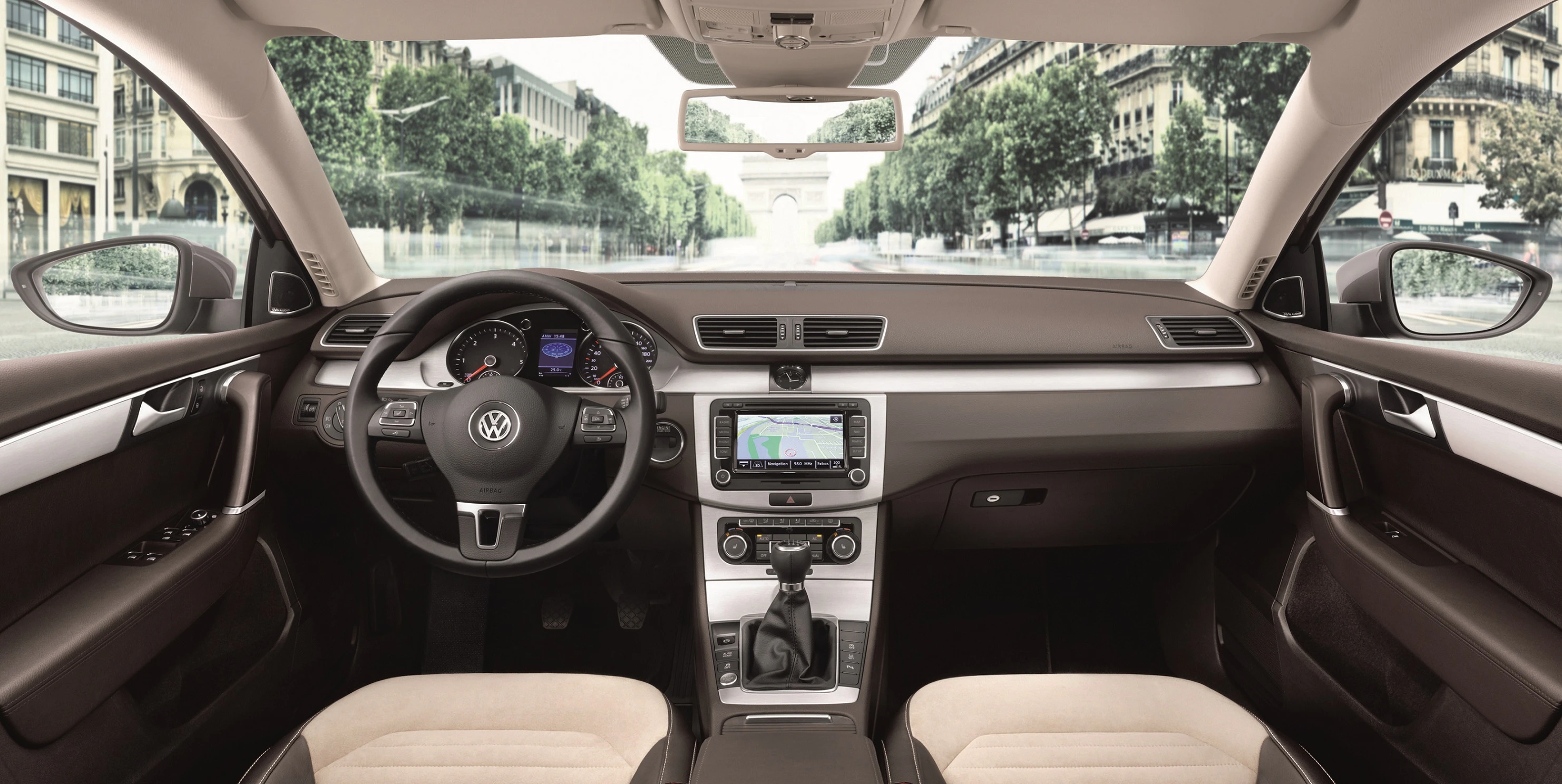 Innenraum eines Autos mit Lederinterieur, Lenkrad und Armaturenbrett mit integriertem Display. Blick aus der Windschutzscheibe auf eine Allee.