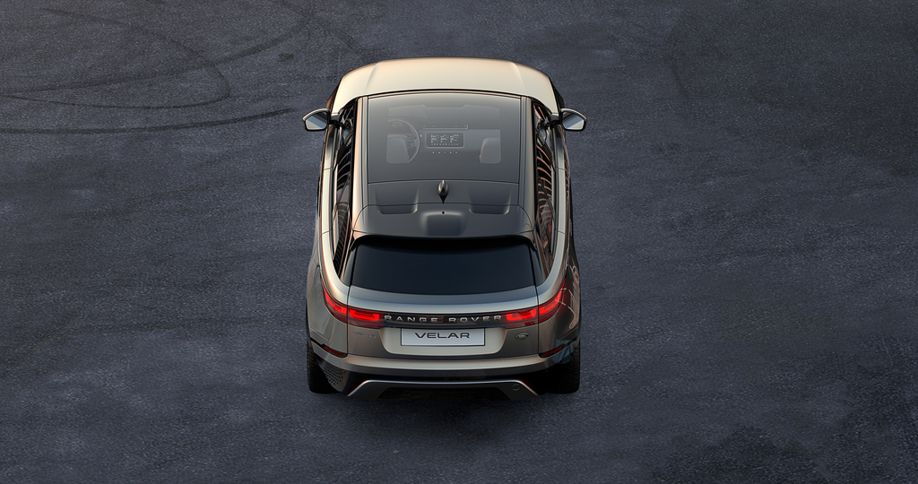 Ansicht eines Range Rover Velar von oben auf grauem Asphalt. Der Wagen ist in einer hellen Farbe lackiert und hat ein Panoramaglasdach.